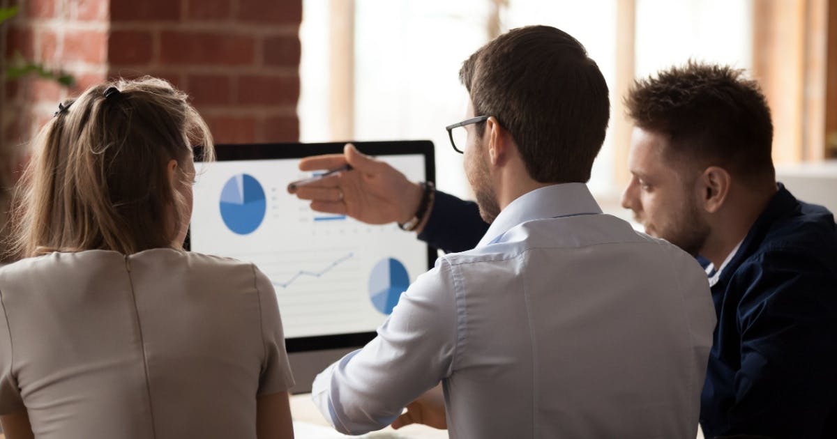  Três pessoas observando um computador com gráficos na tela.