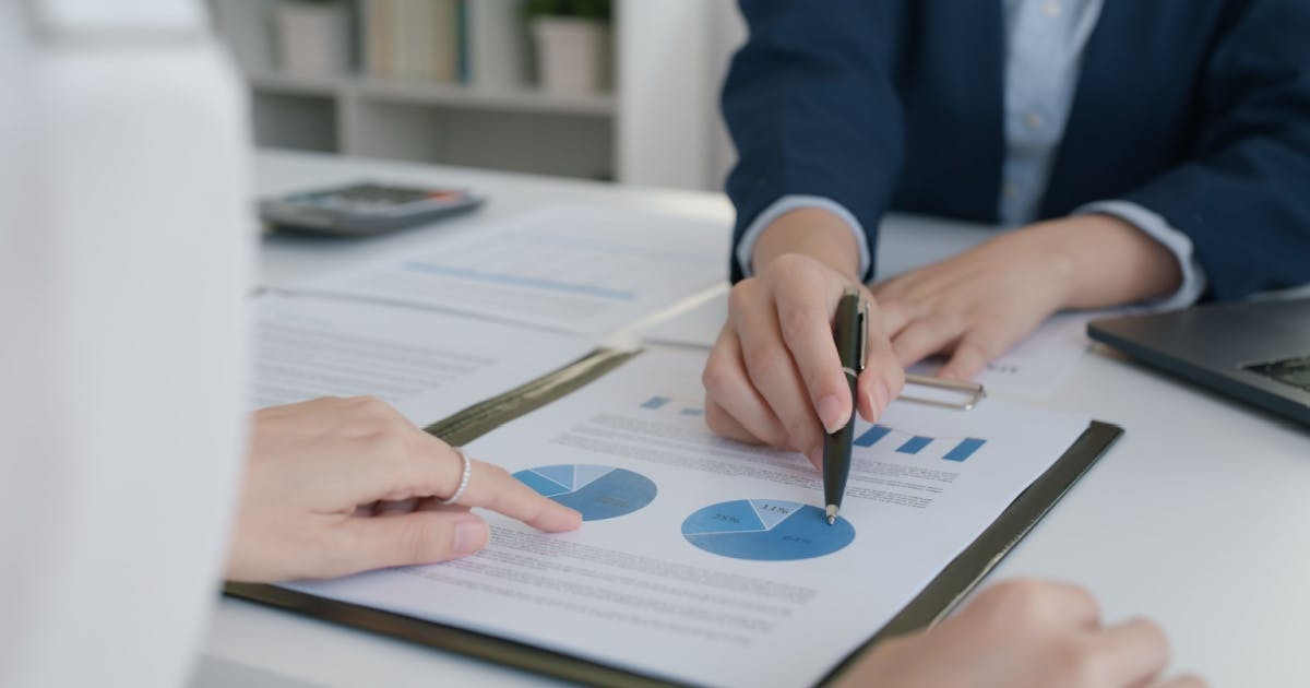 Duas pessoas analisam um documento com gráficos, uma delas aponta com uma caneta para a folha.