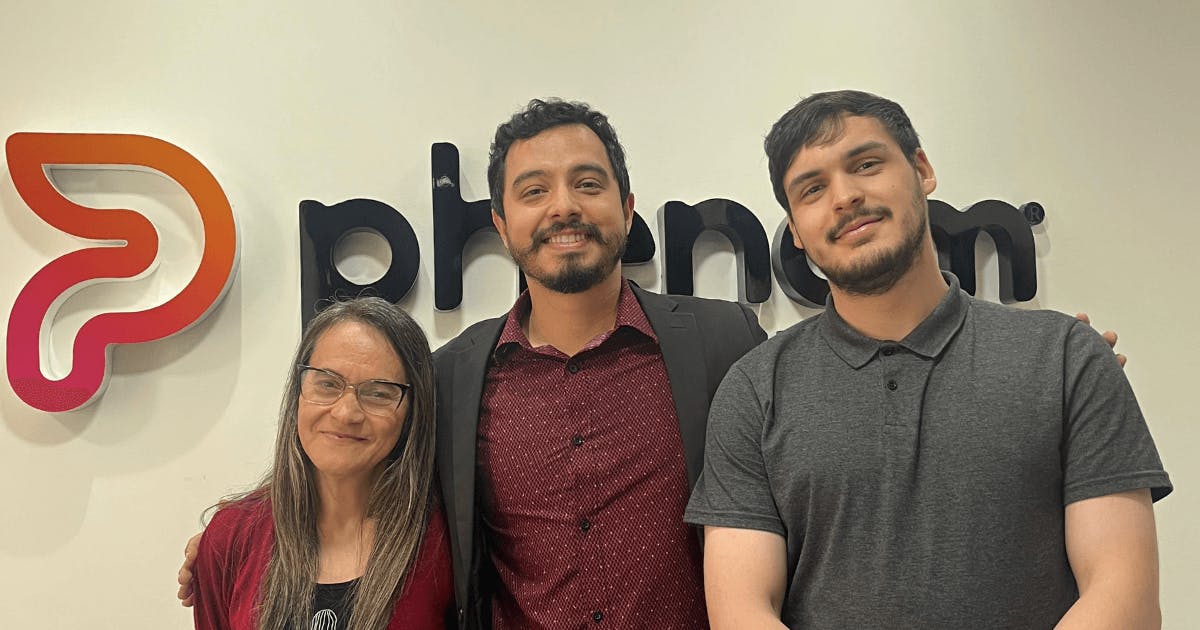Três pessoas em pé diante do logo da Phenom.