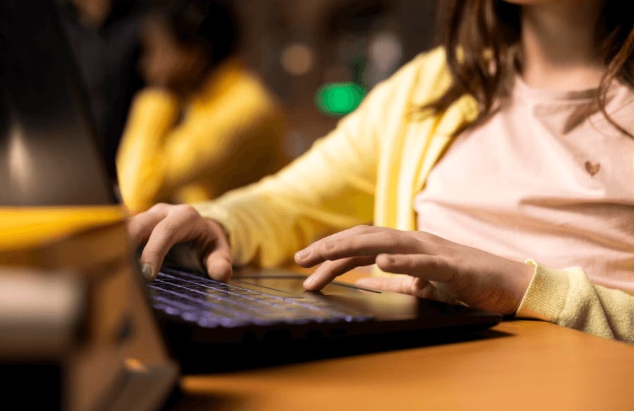 Pessoa usando um laptop em ambiente de estudo ou trabalho, com foco nas mãos e na tela do computador, em ambiente com iluminação amena e aconchegante.