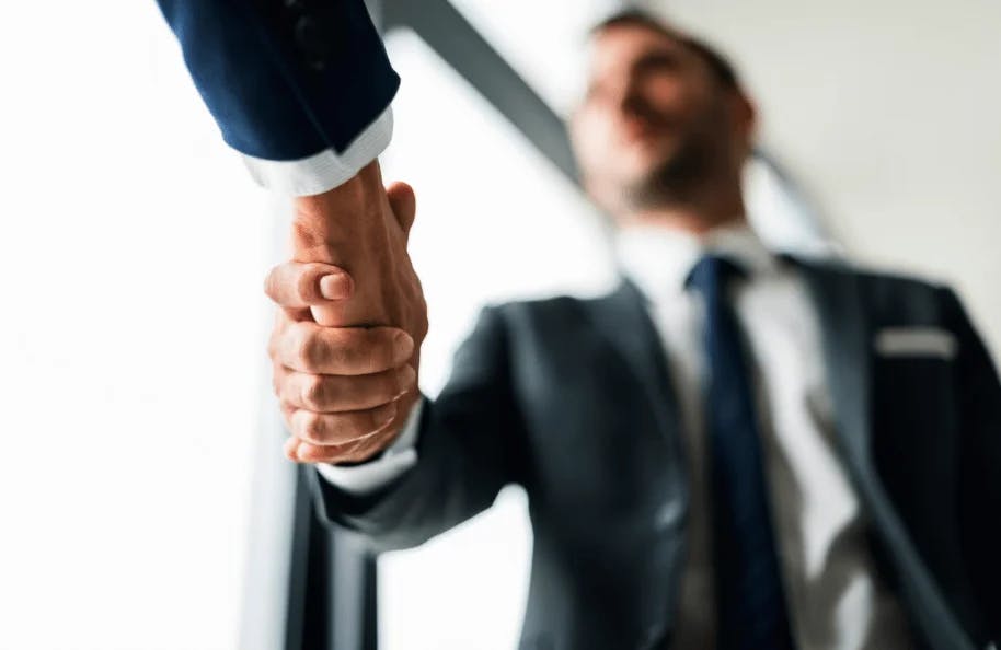 Imagem de dois empresários apertando as mãos em um ambiente corporativo, simbolizando acordo, parceria ou fechamento de negócio.