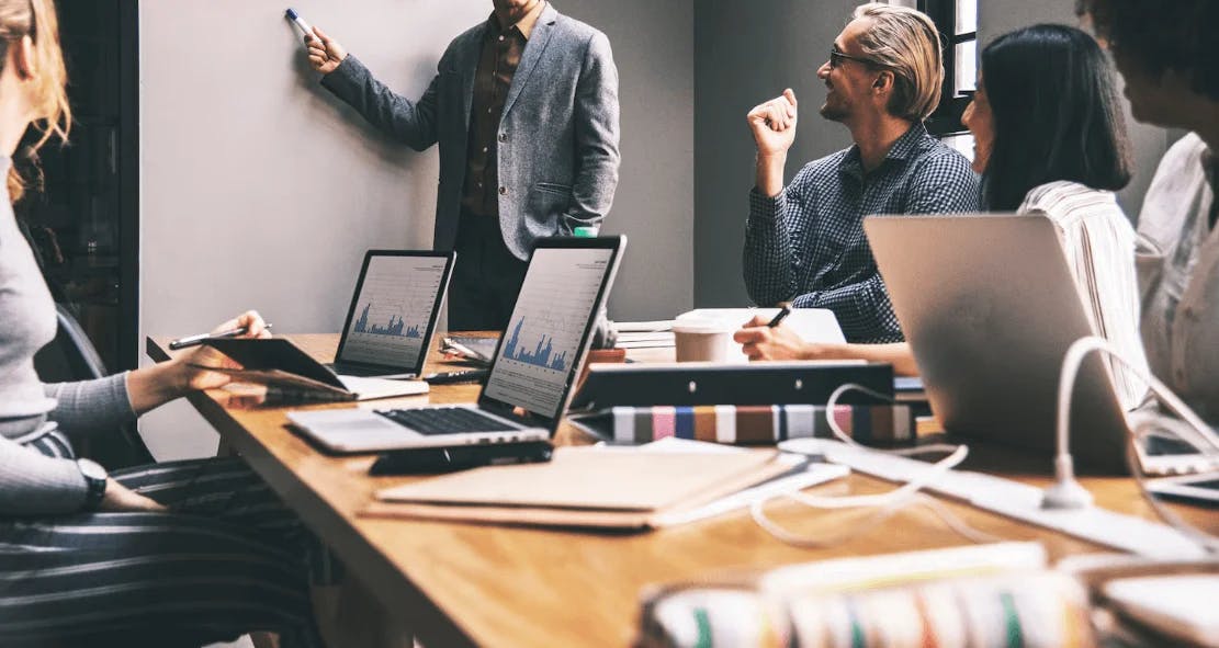 Reunião de negócios com profissionais usando laptops e projetor em sala de reunião moderna.