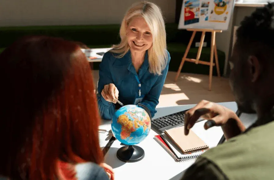 Professora sorridente em sala de aula, apontando para um globo terrestre sobre a mesa enquanto estudantes observam e anotam em cadernos, criando atividade educativa de geografia