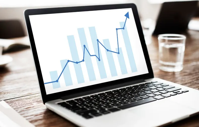 Notebook na mesa com gráfico de crescimento em barras e linha ascendente na tela, sugerindo análise de dados, desempenho e planejamento financeiro