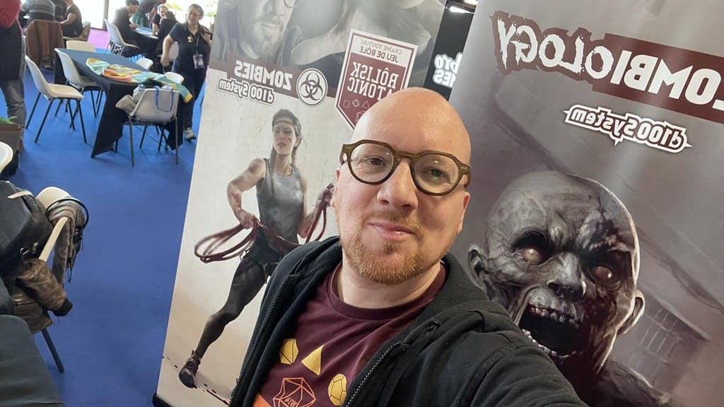 Damien Coltice devant une affiche de Zombiology lors d'un salon