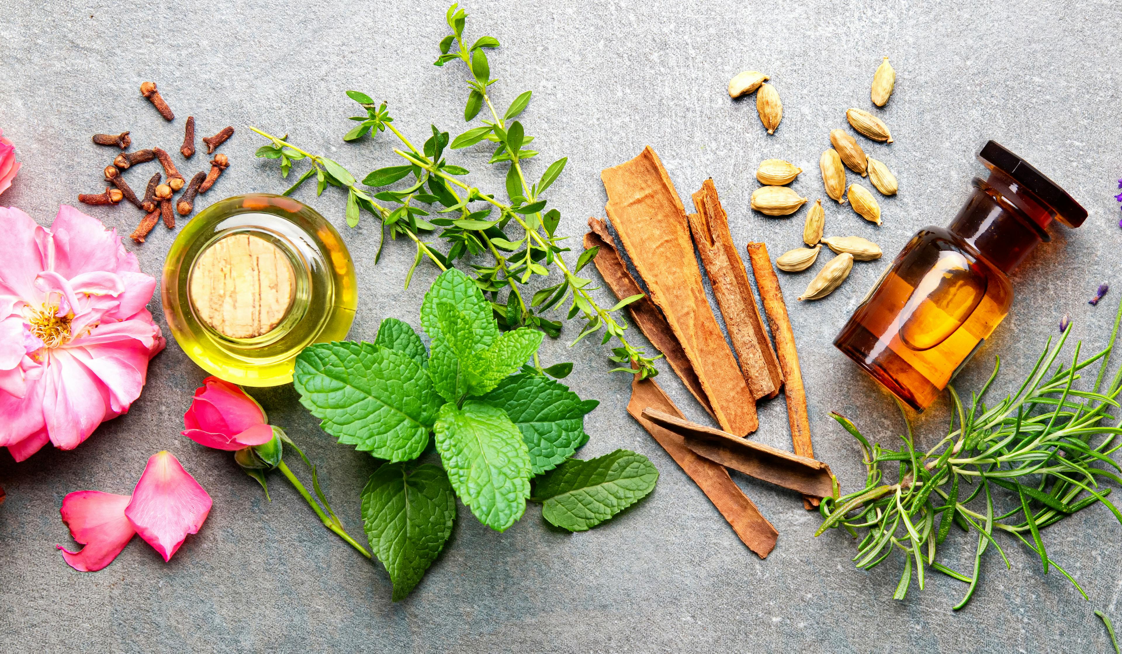 Bottles of essential oil with rosemary, thyme, cinnamon sticks, cardamom, mint, lavender, and rose petals