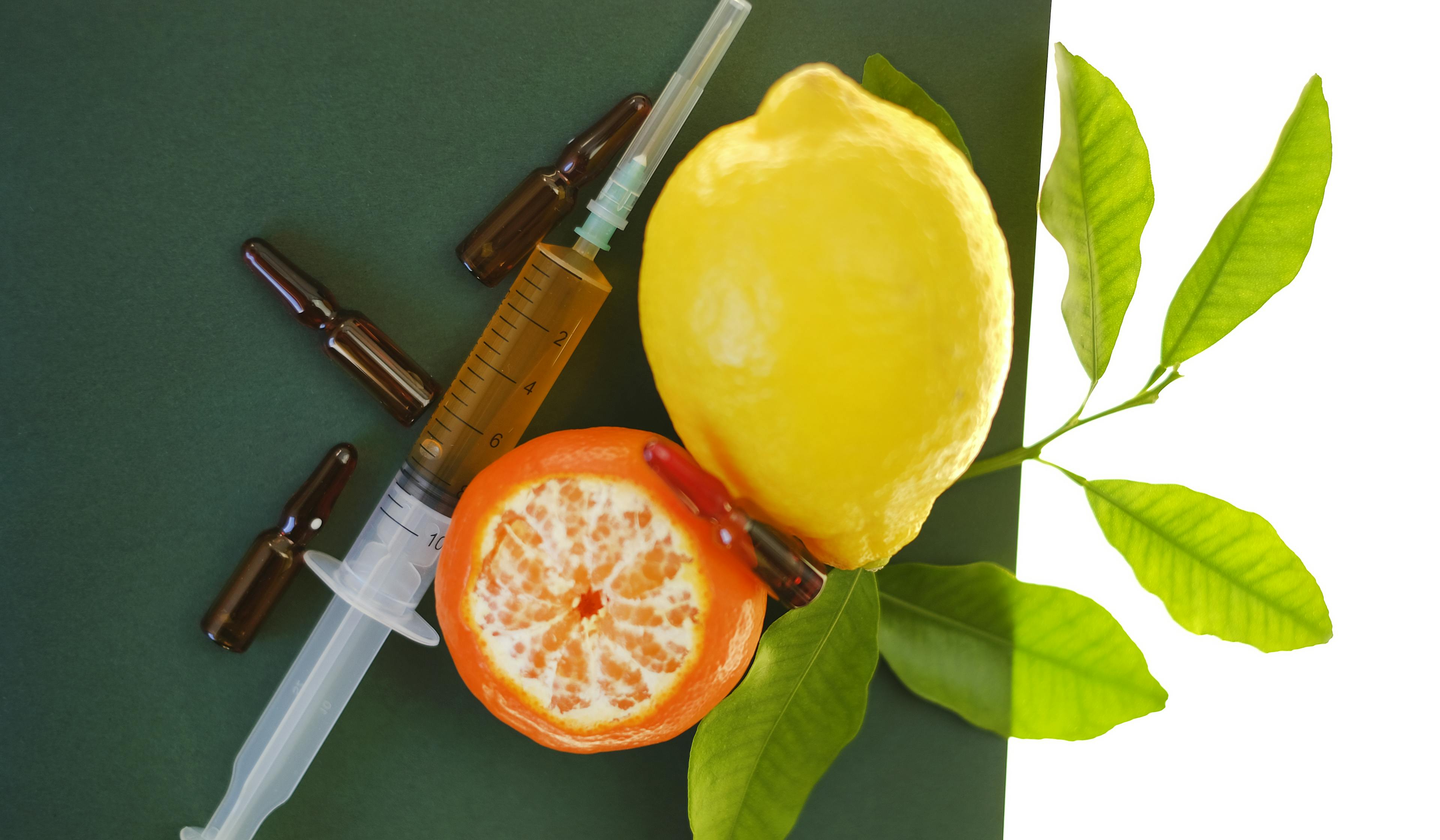 syringe with injection solution and lemons fruits on green background