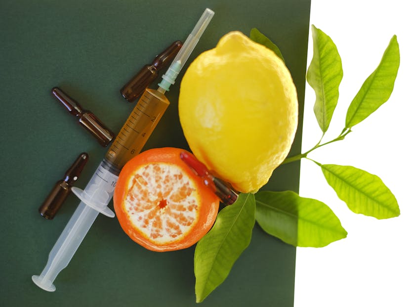 syringe with injection solution and lemons fruits on green background
