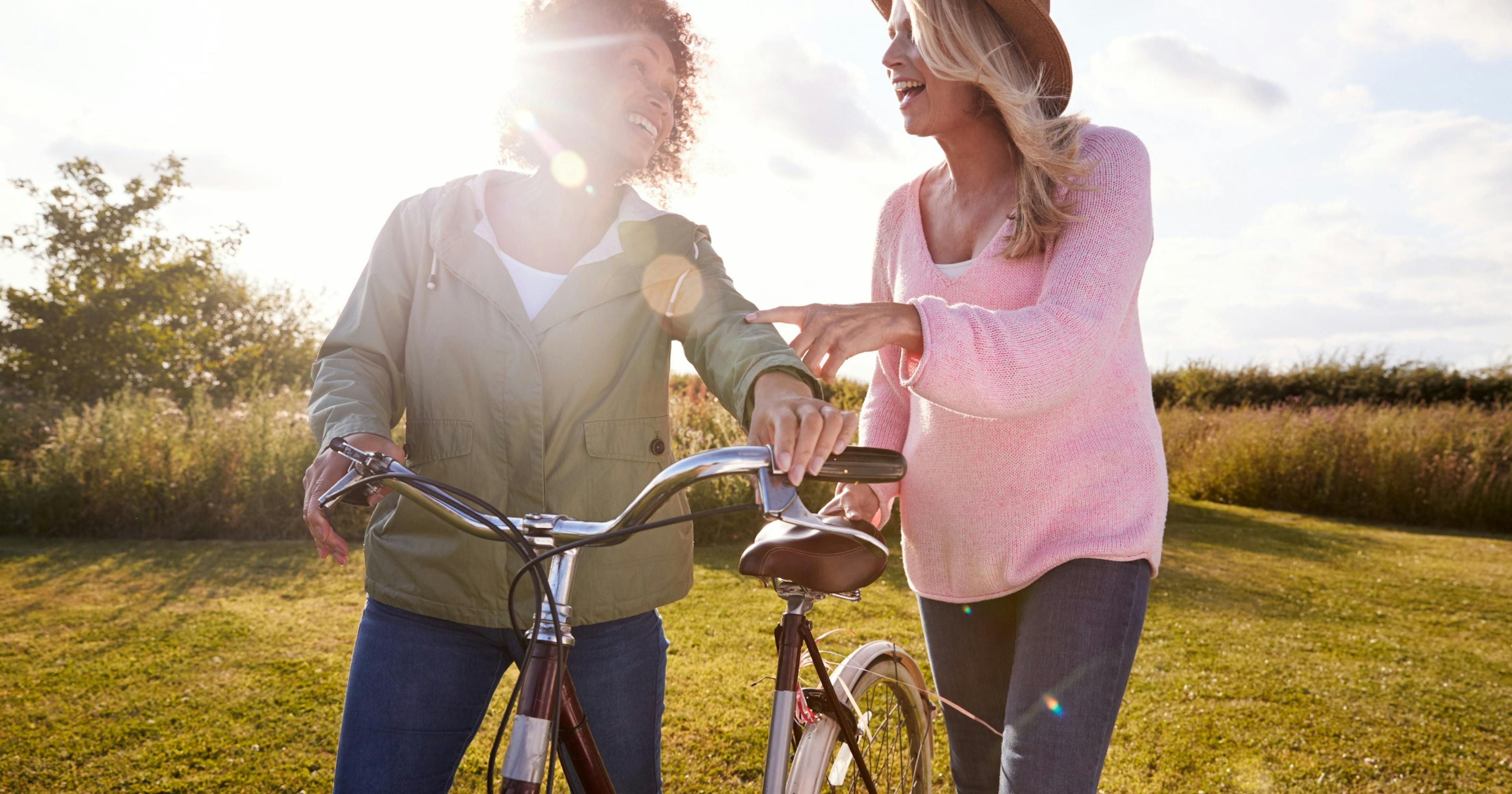 Two mature women friends walking through a field with a bike.