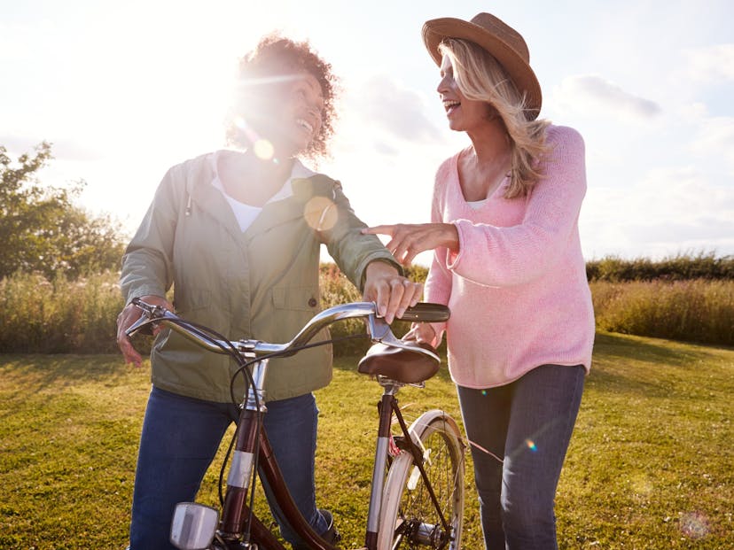 Two mature women friends walking through a field with a bike.