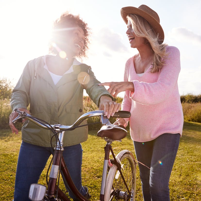 Two mature women friends walking through a field with a bike.