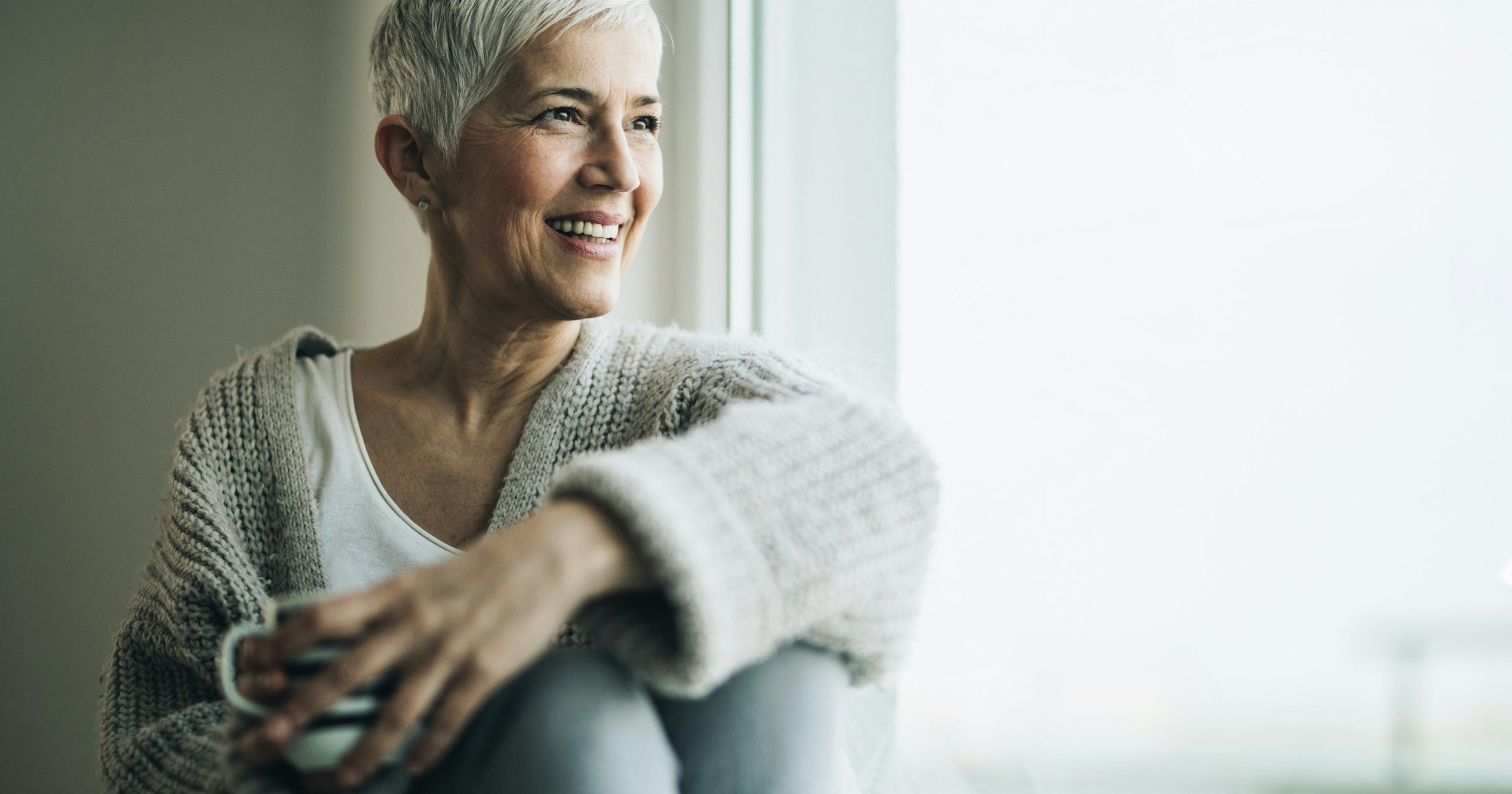 happy mature woman sitting by window with coffee