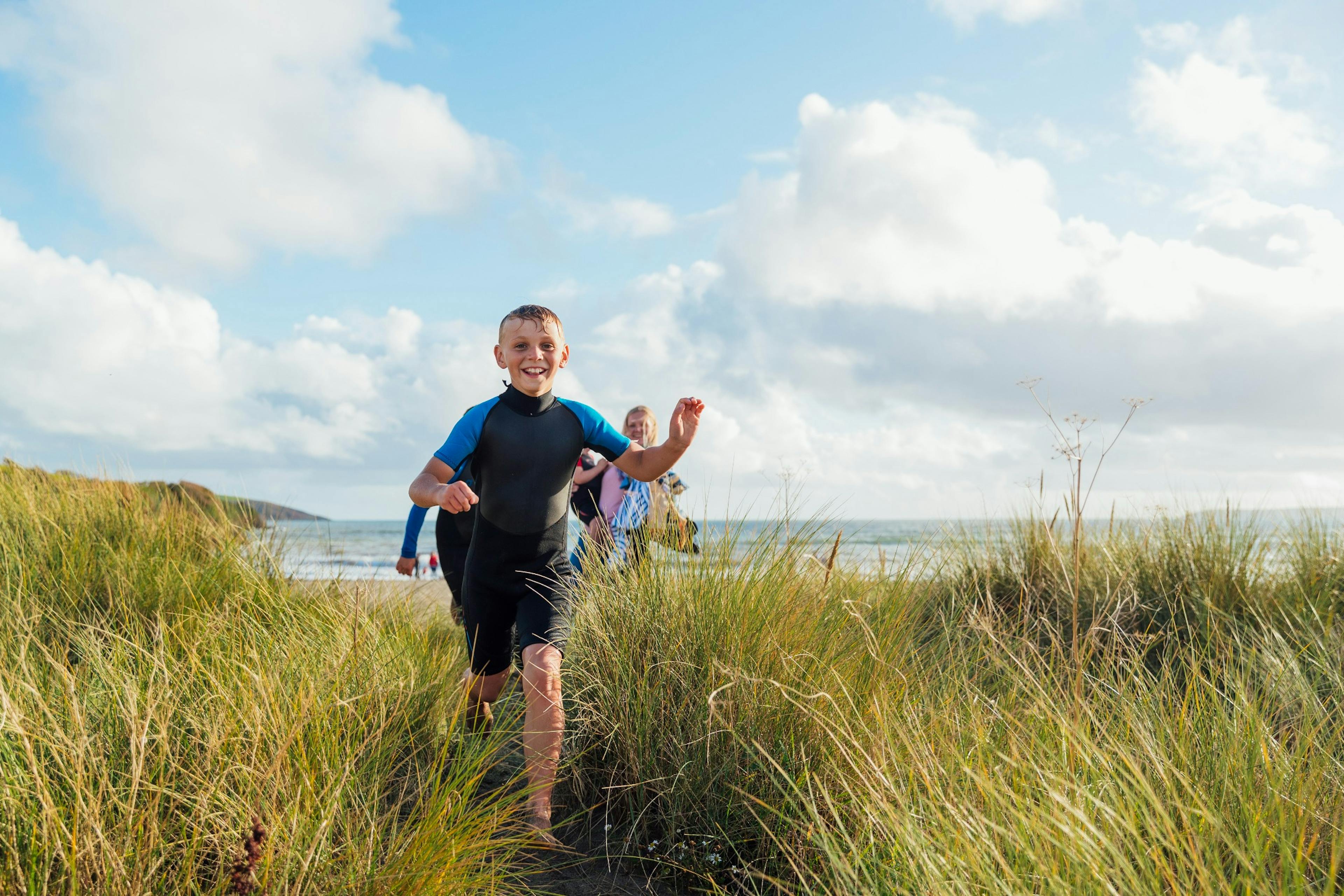 young boy running through tall grasss near a beach