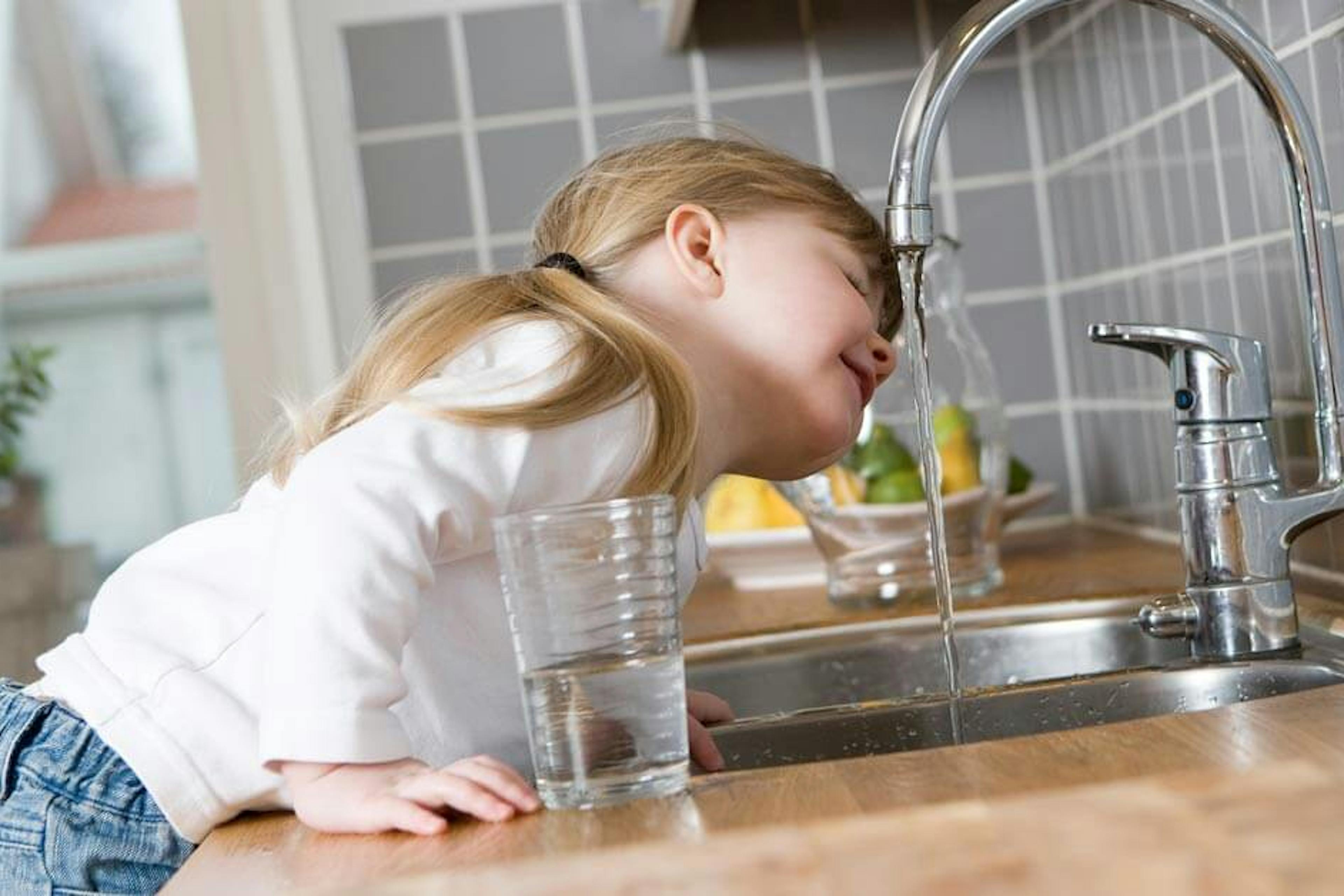 small girl drinking water from a faucet