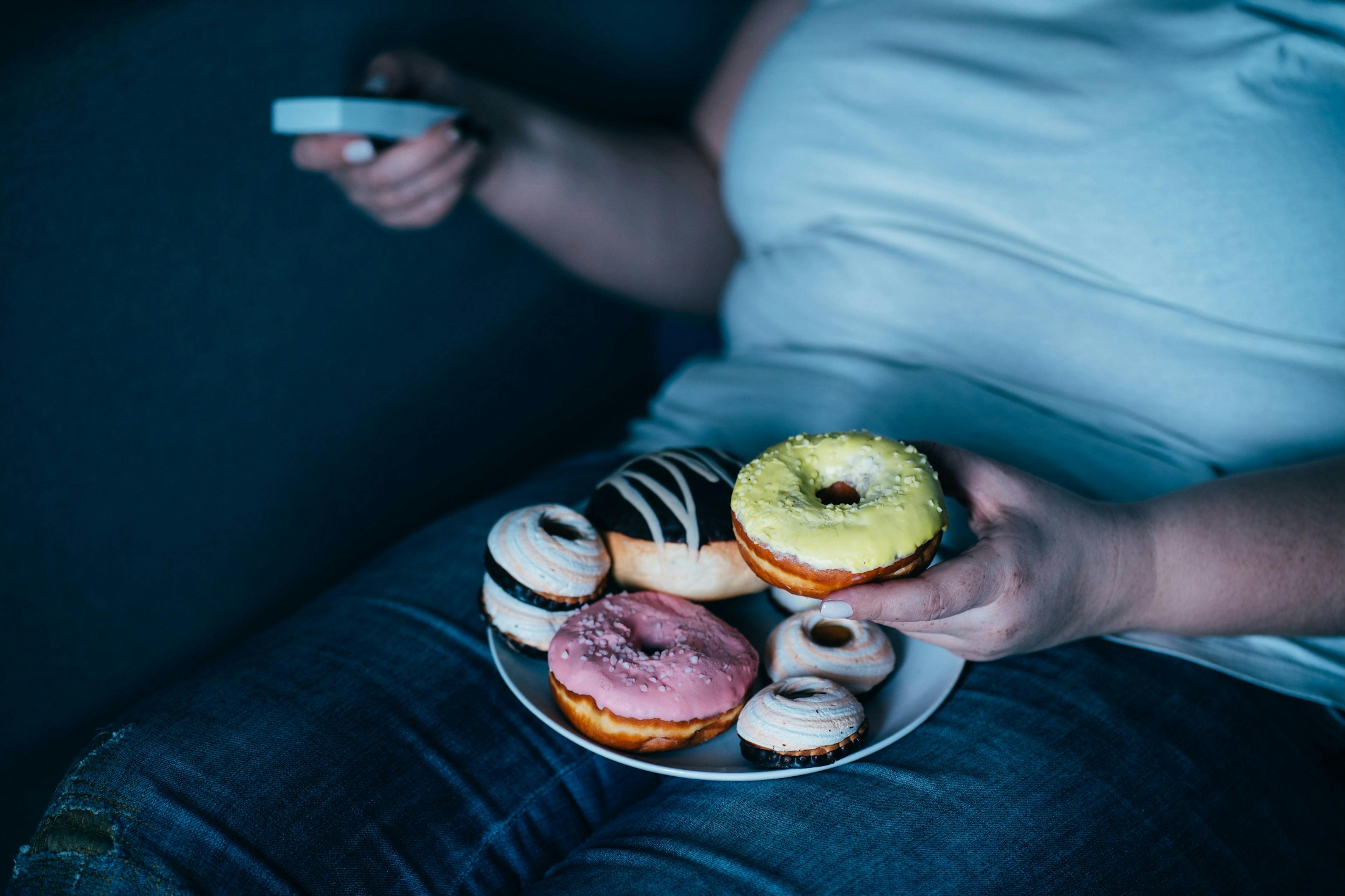 overweight woman eating doughnuts on the couch