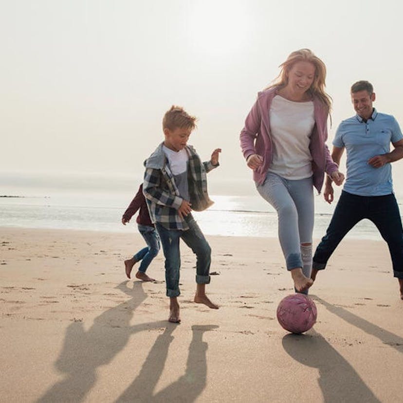 Family playing soccer on the beach.