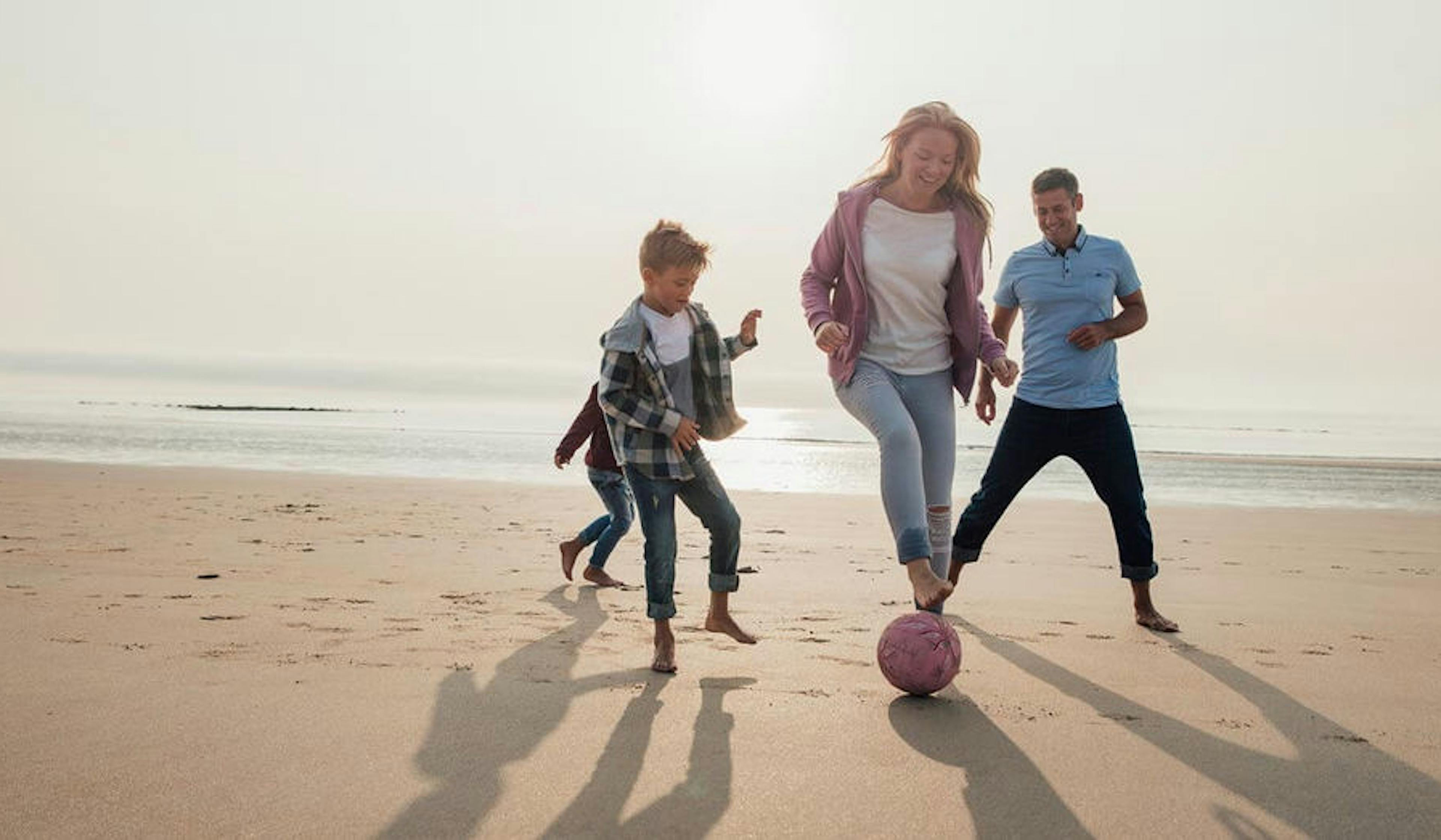 Family playing soccer on the beach.