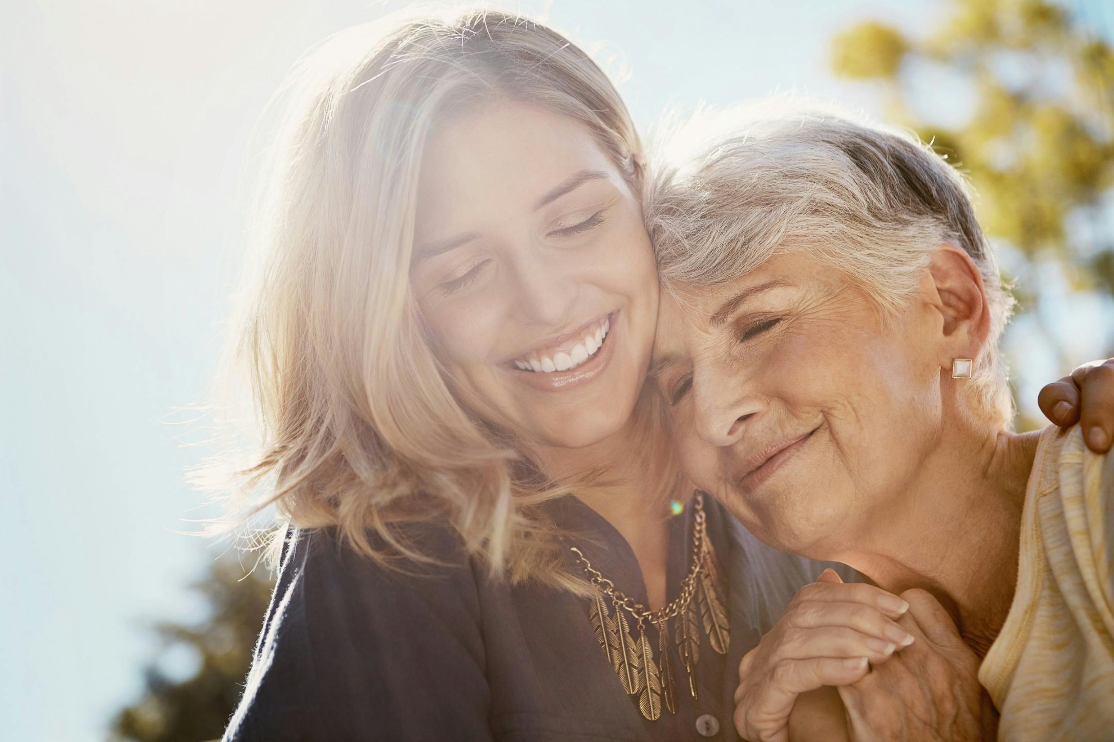 middle age daughter and older mom hug in sun