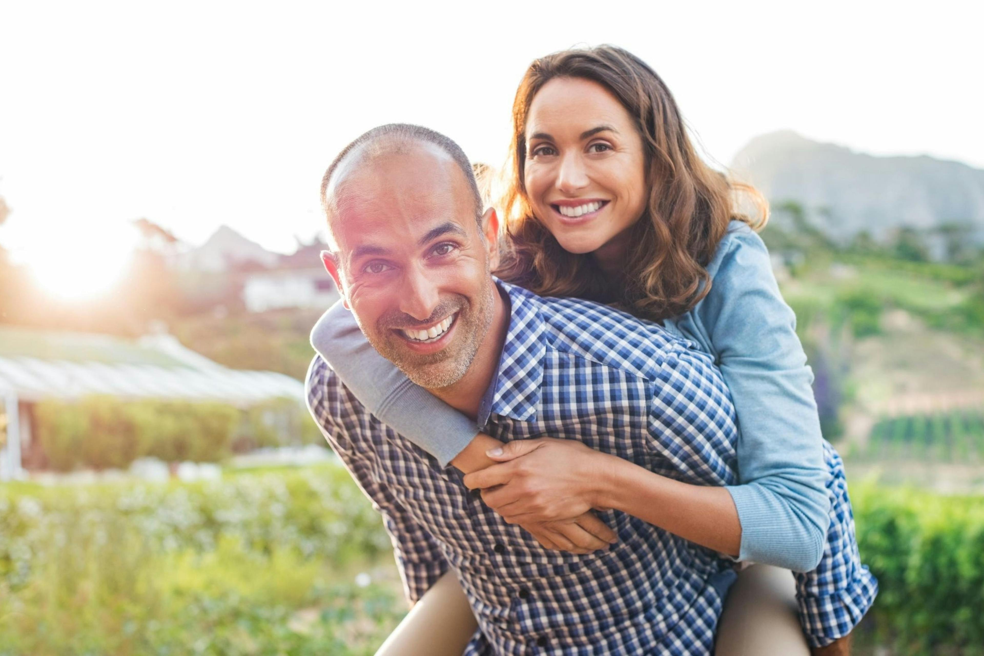 middle-aged couple taking a piggyback ride through a field