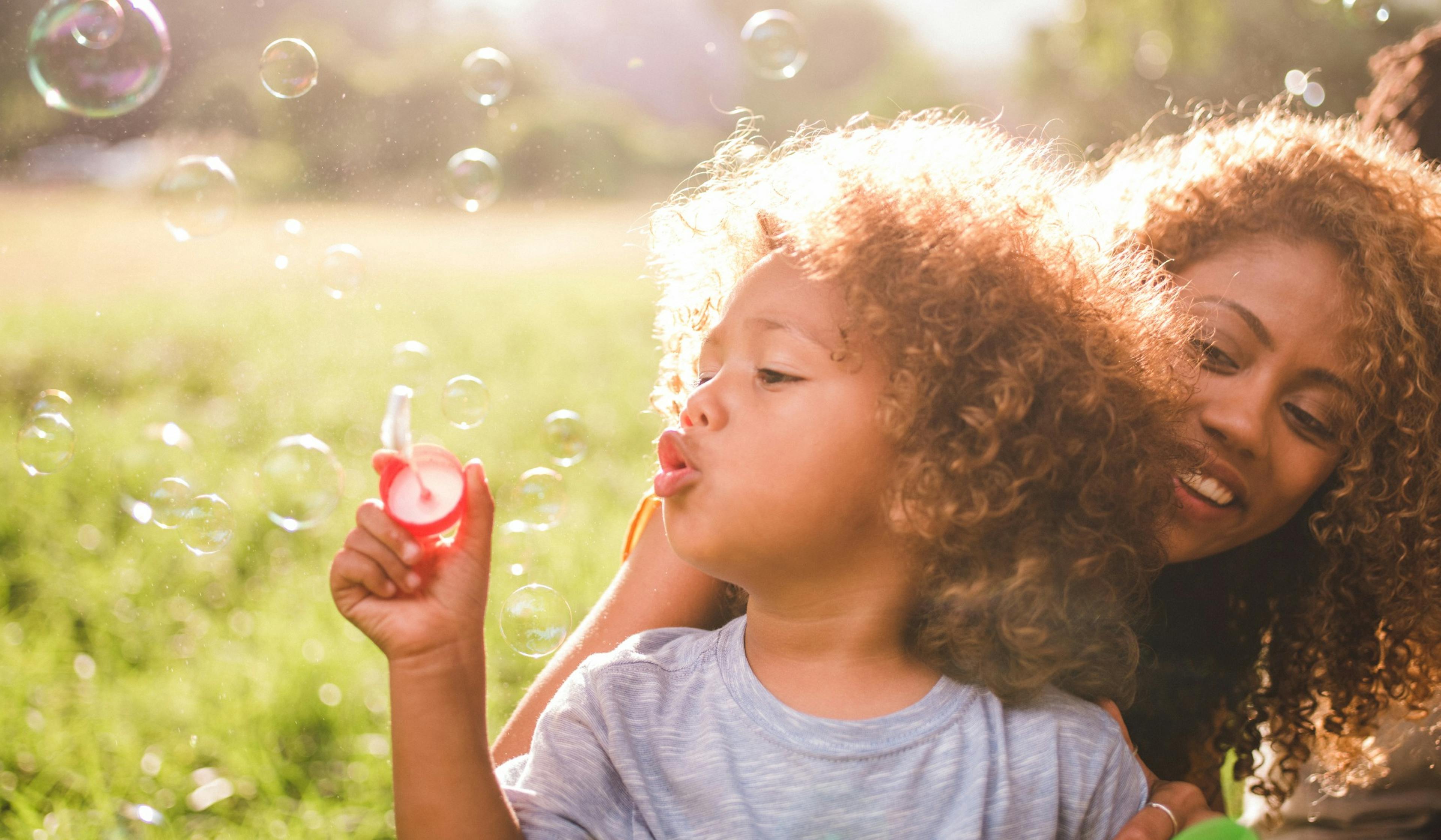 young boy and mom blow bubbles outside.