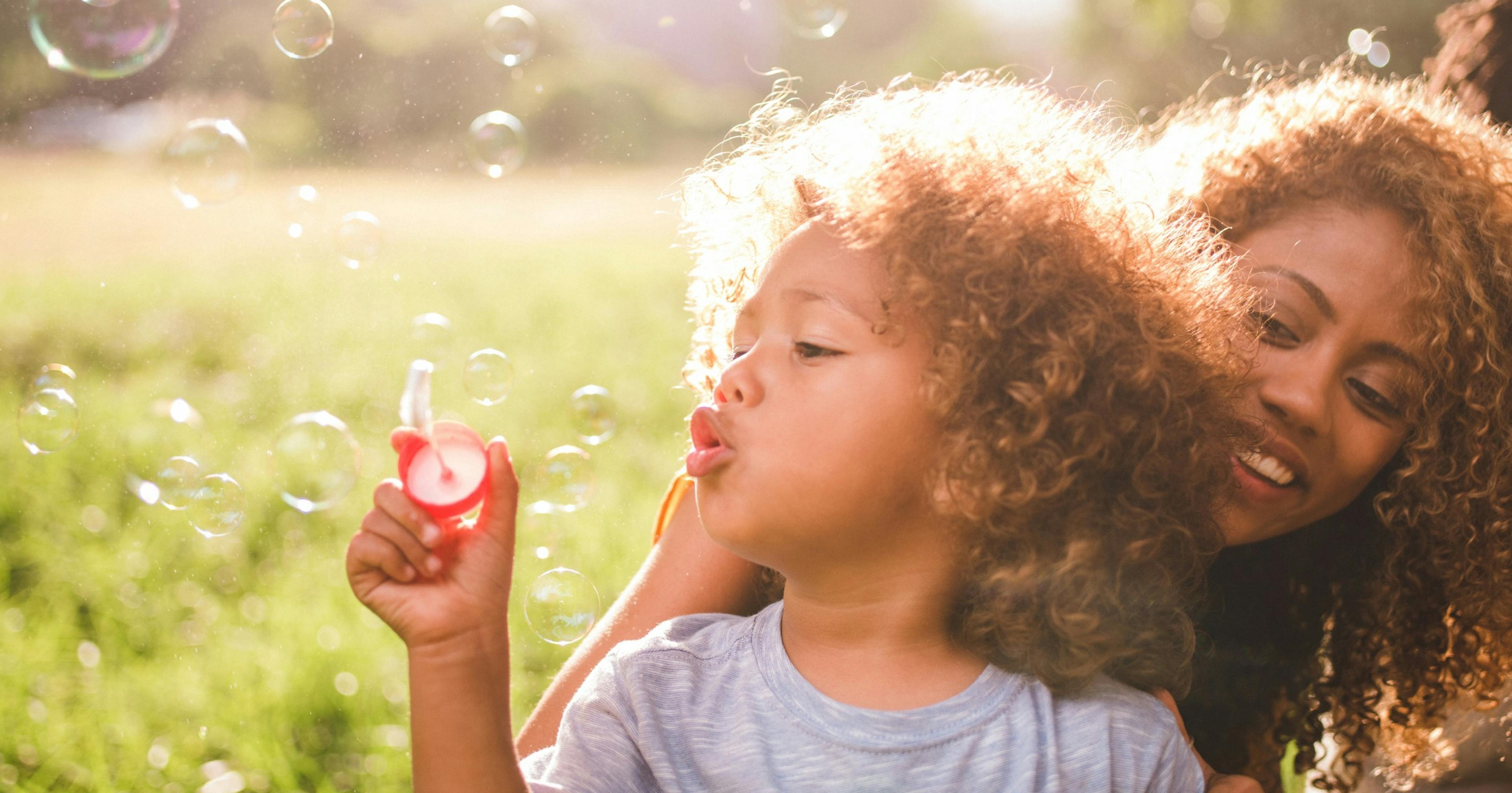 young boy and mom blow bubbles outside.