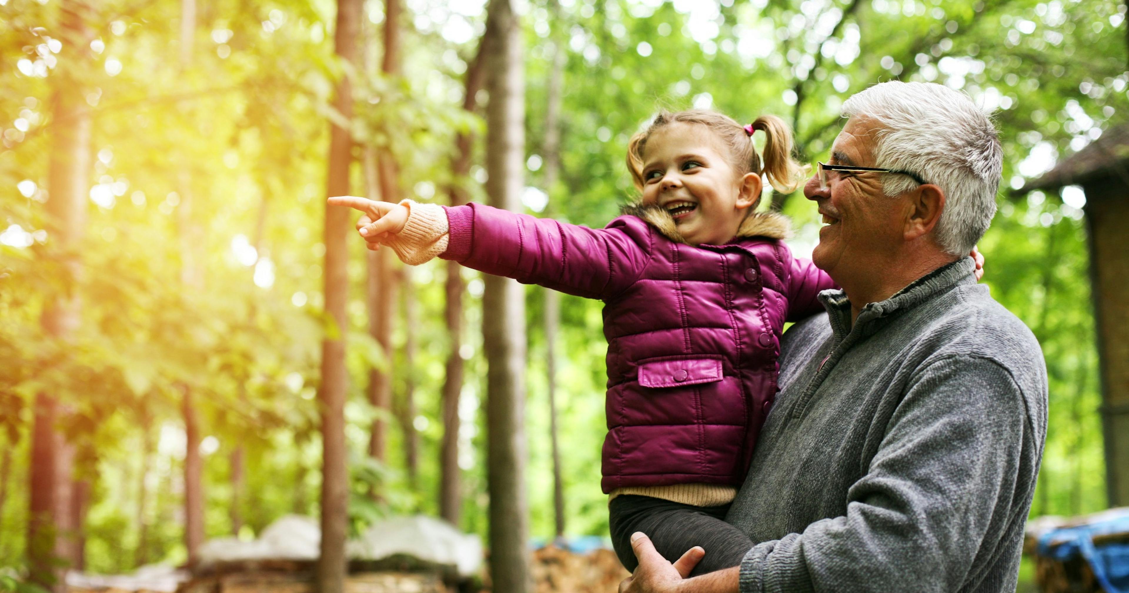 little girl showing her grandfather something in the woods