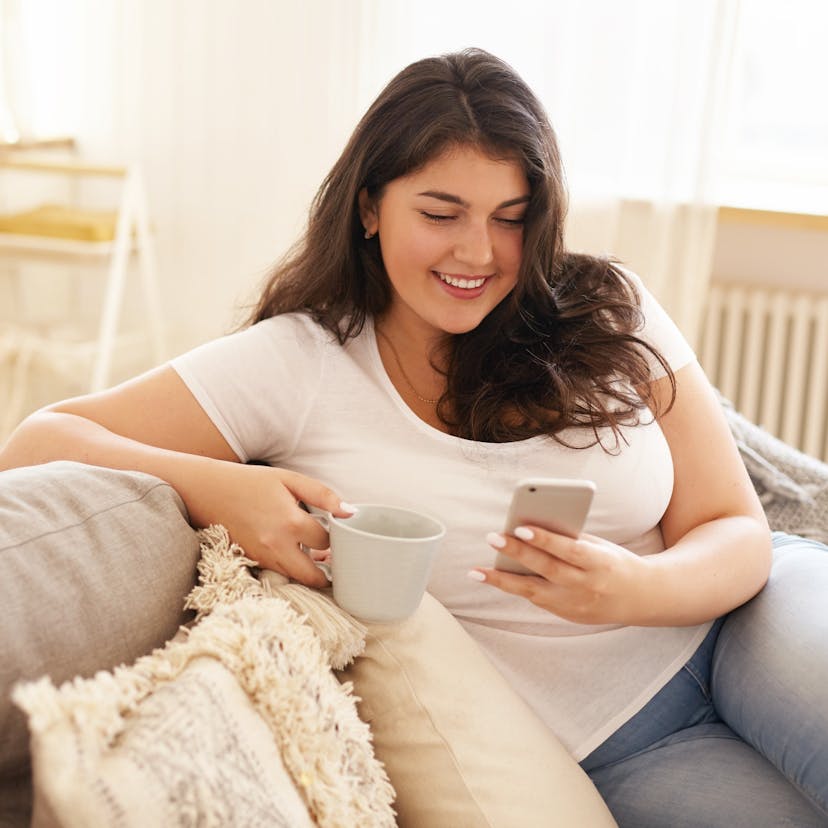 Heavier woman using phone and drinking coffee