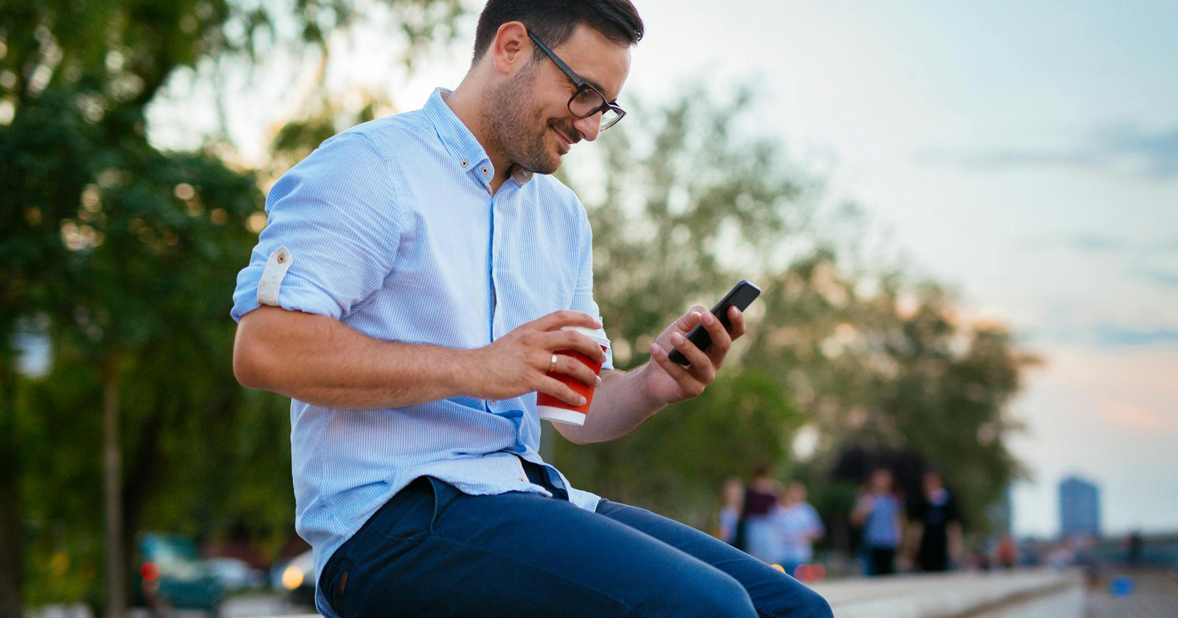 happy professional man outside looking at phone and holding a coffee.jpg