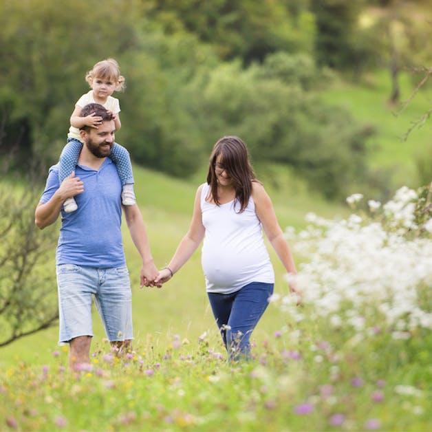 pregnant mom, husband and daughter walking through a field