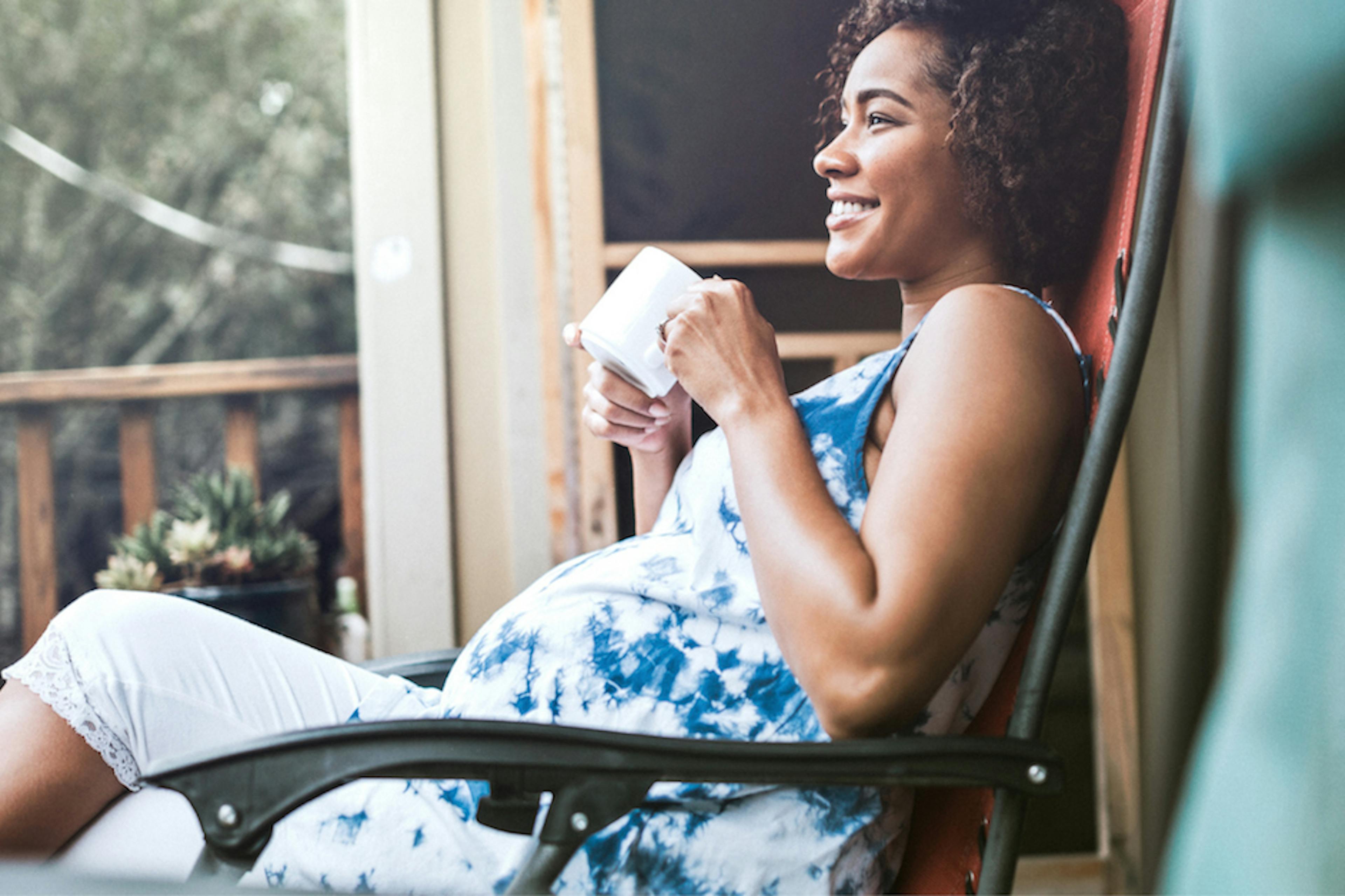 pregnant lady sitting in chair outside drinking coffee