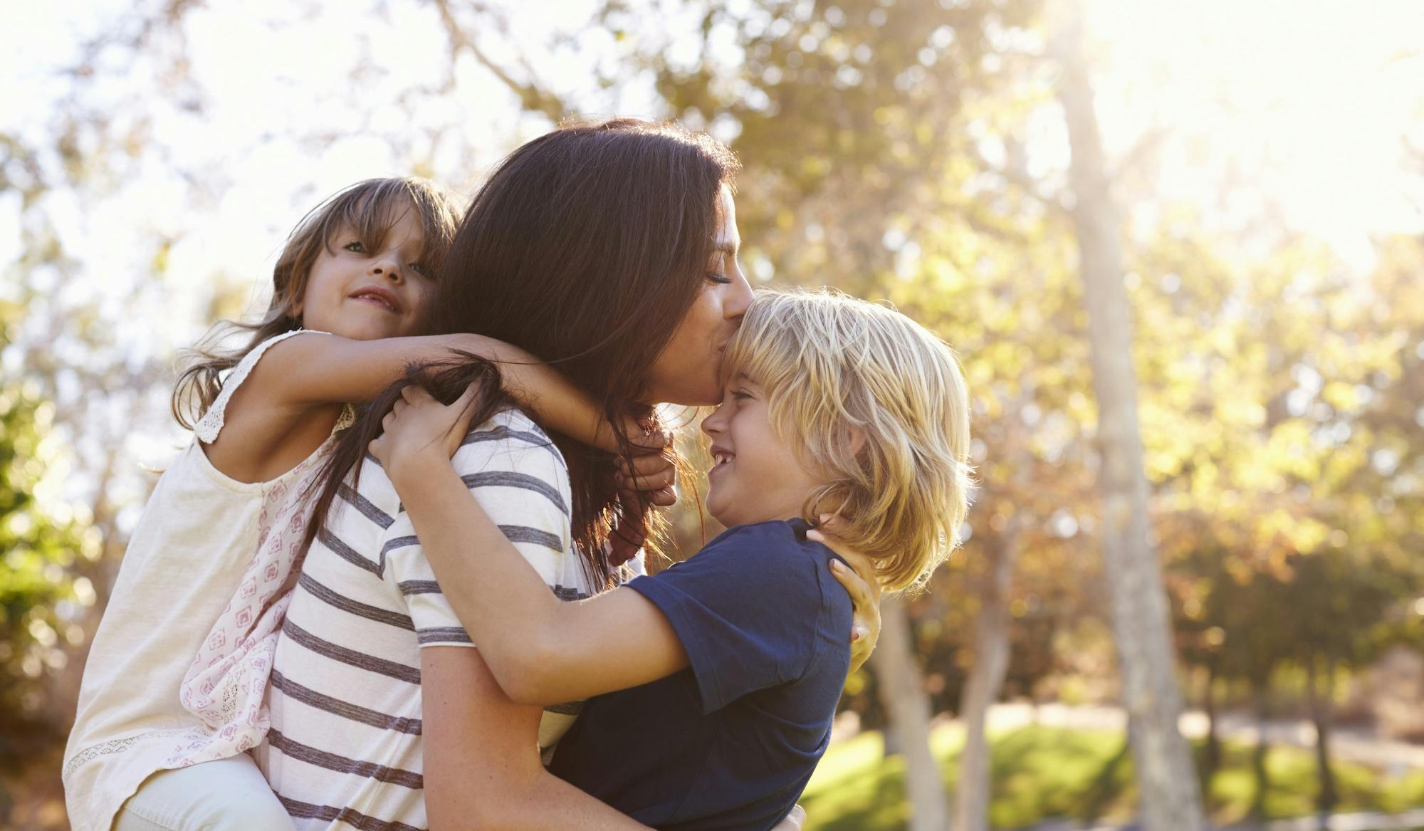 Mother Carrying Son And Daughter As They Play In Park