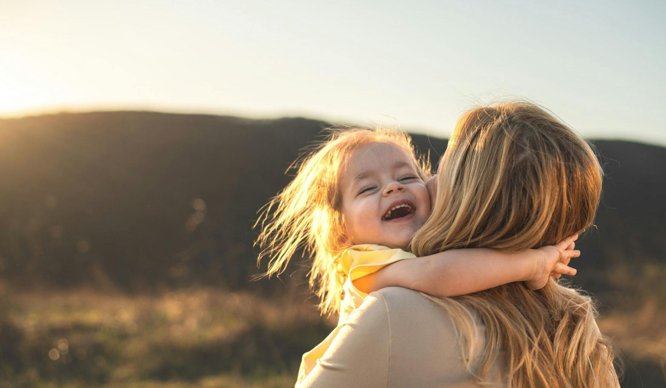 Happy girl kid hugging mom in the nature