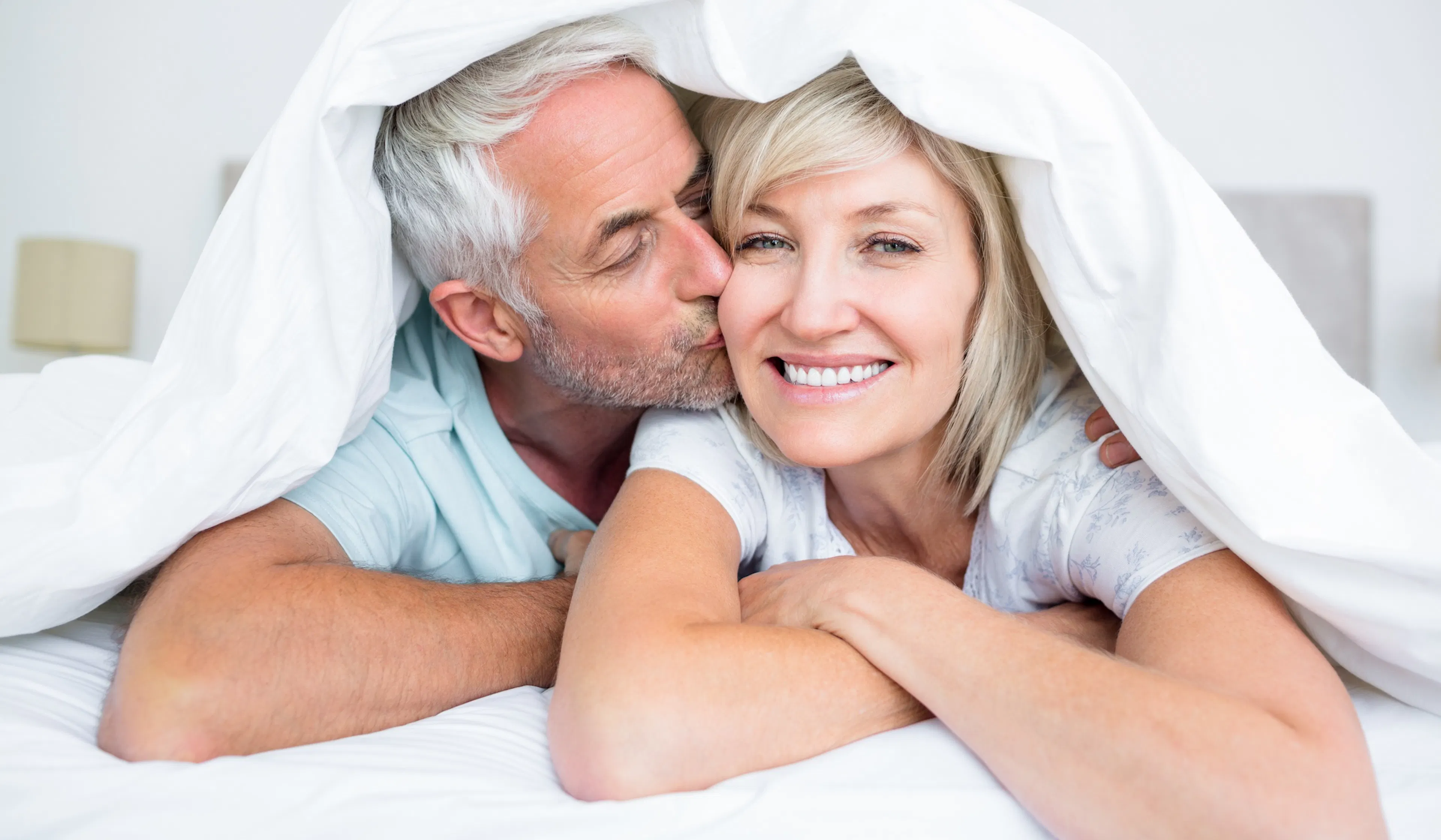 mature man kissing womans cheek in bed