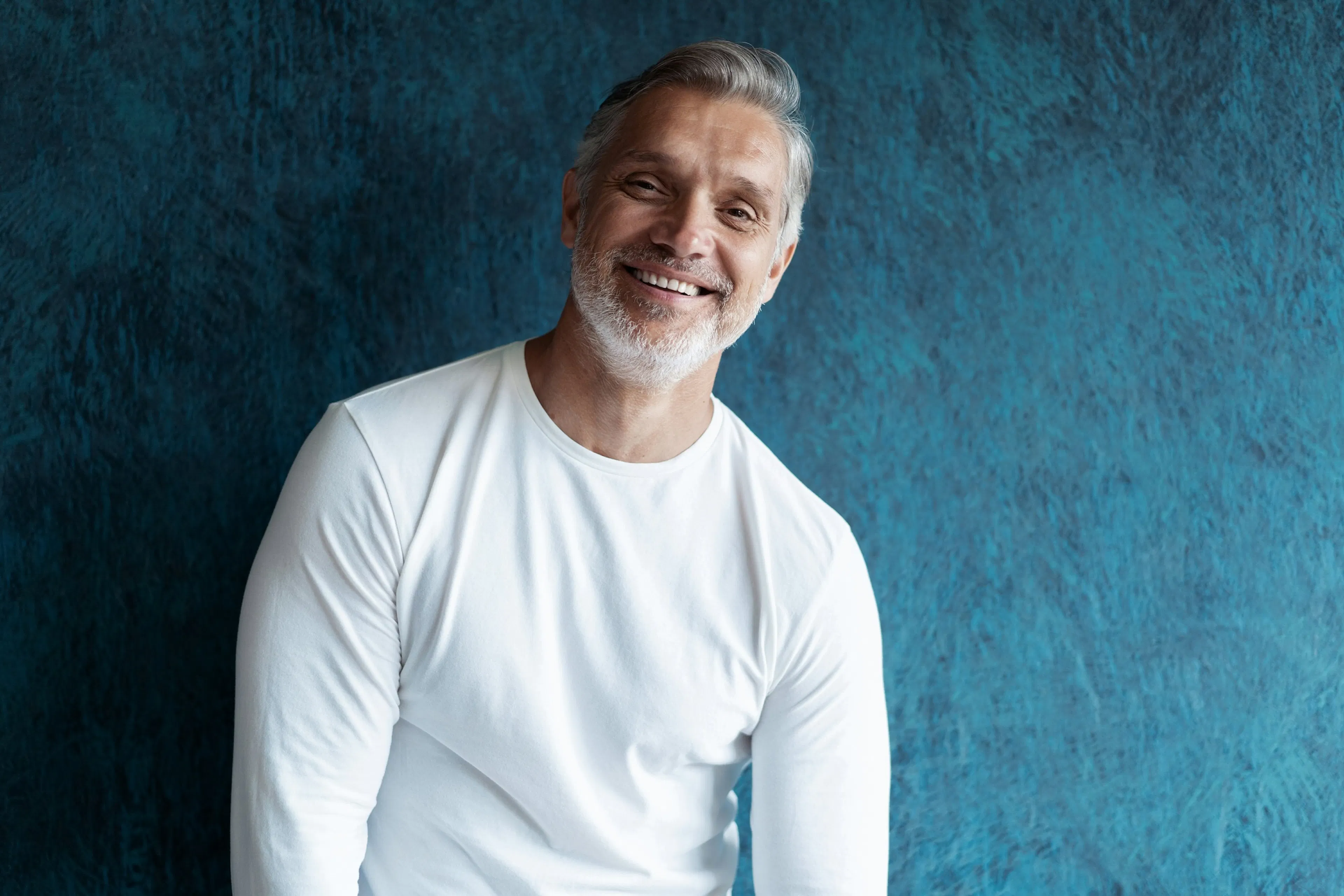 grey haired man smiling against blue wall