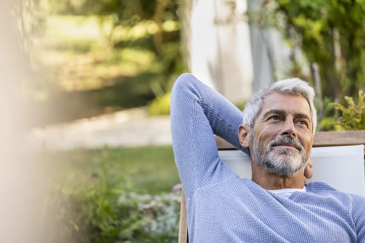 Thoughtful mature man with hands behind head sitting on deckchair