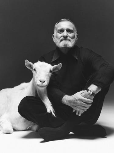 Black and white photo of designer Ward Bennett, sitting on the floor next to a white goat.
