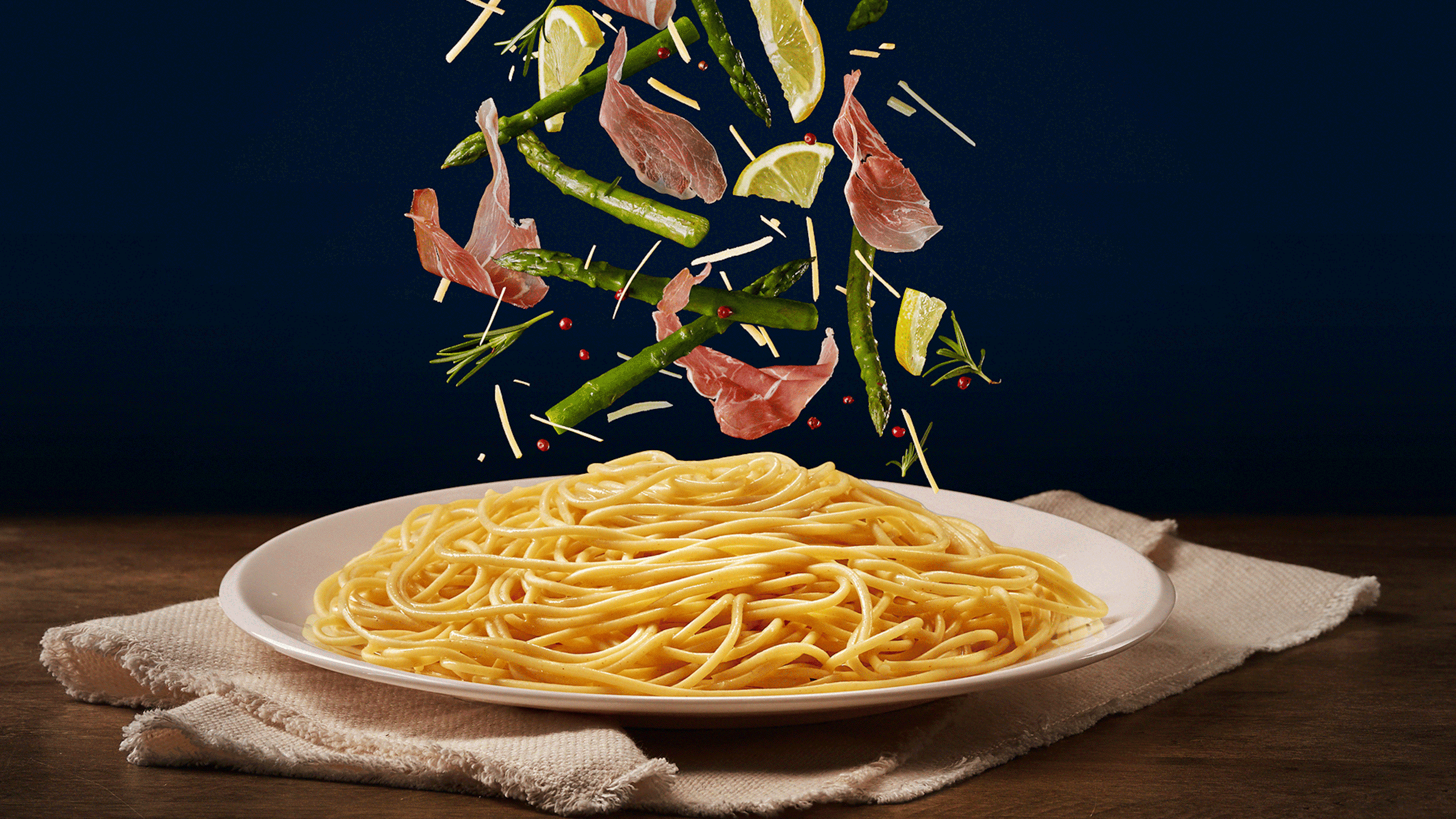 Gif com os ingredientes (aspargos, limão e presunto parma) caindo no macarrão espaguete de várias formas diferentes