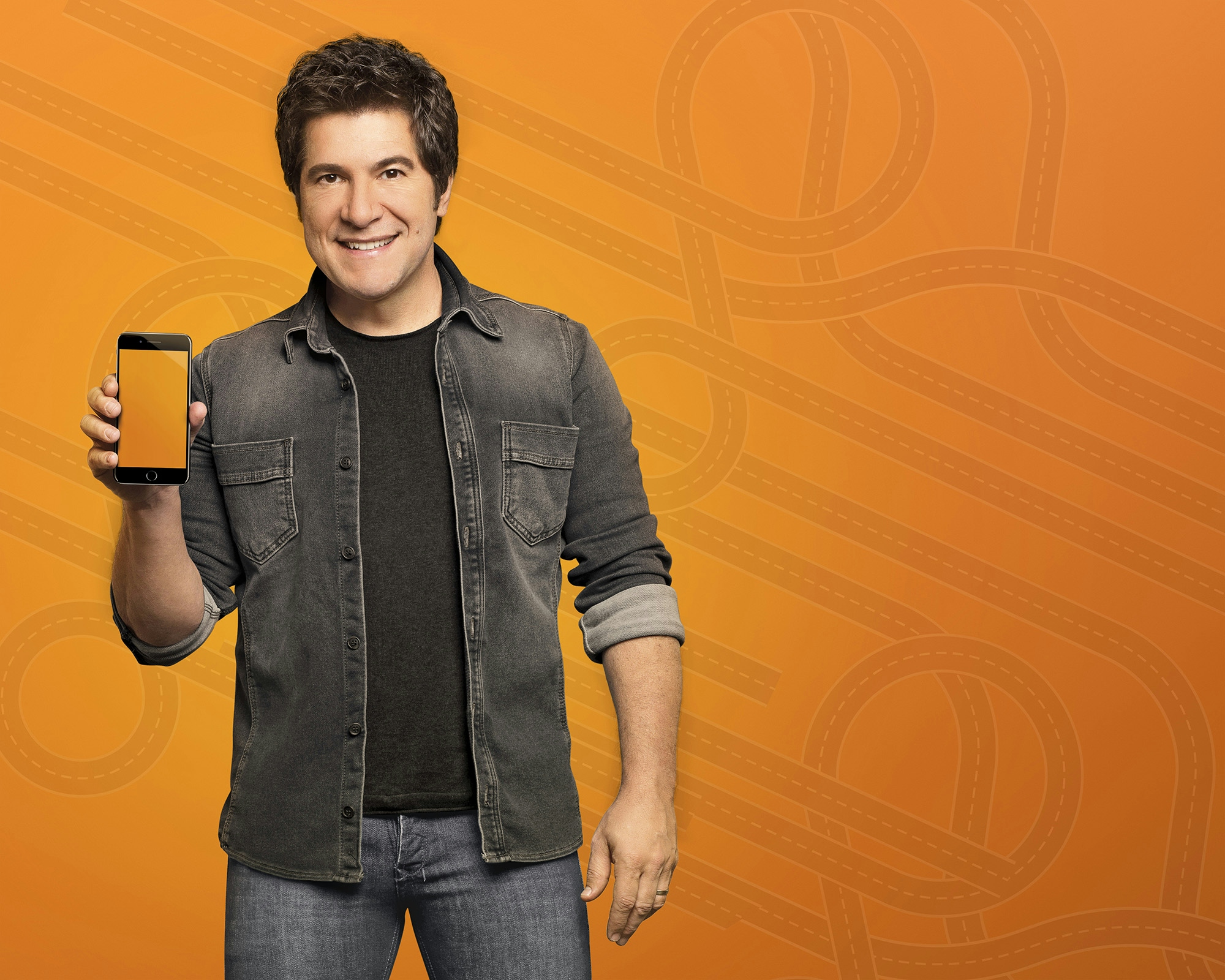 Cantor Daniel segurando um celular em um fundo laranja com desenho de estrada