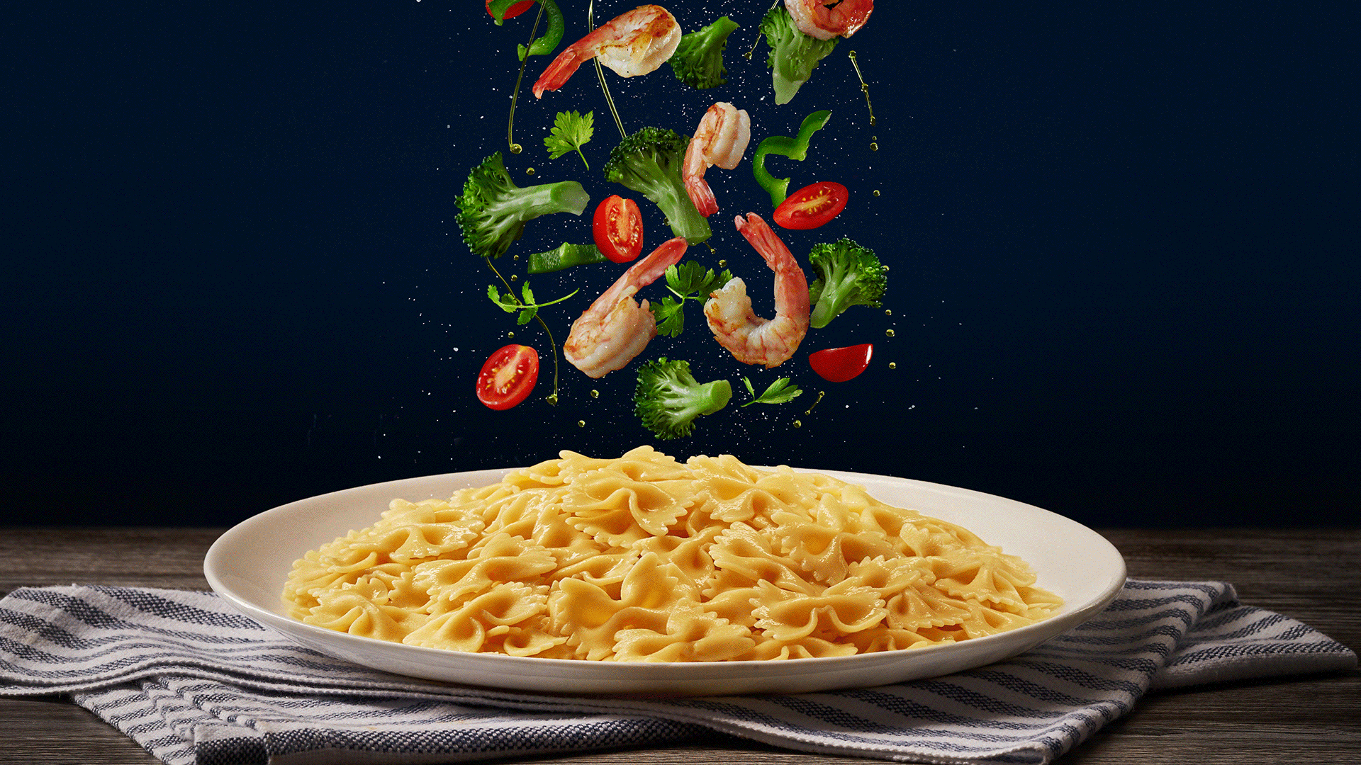 Gif com os ingredientes (brócolis, tomates cereja, azeite e camarão) caindo no macarrão gravata de várias formas diferentes