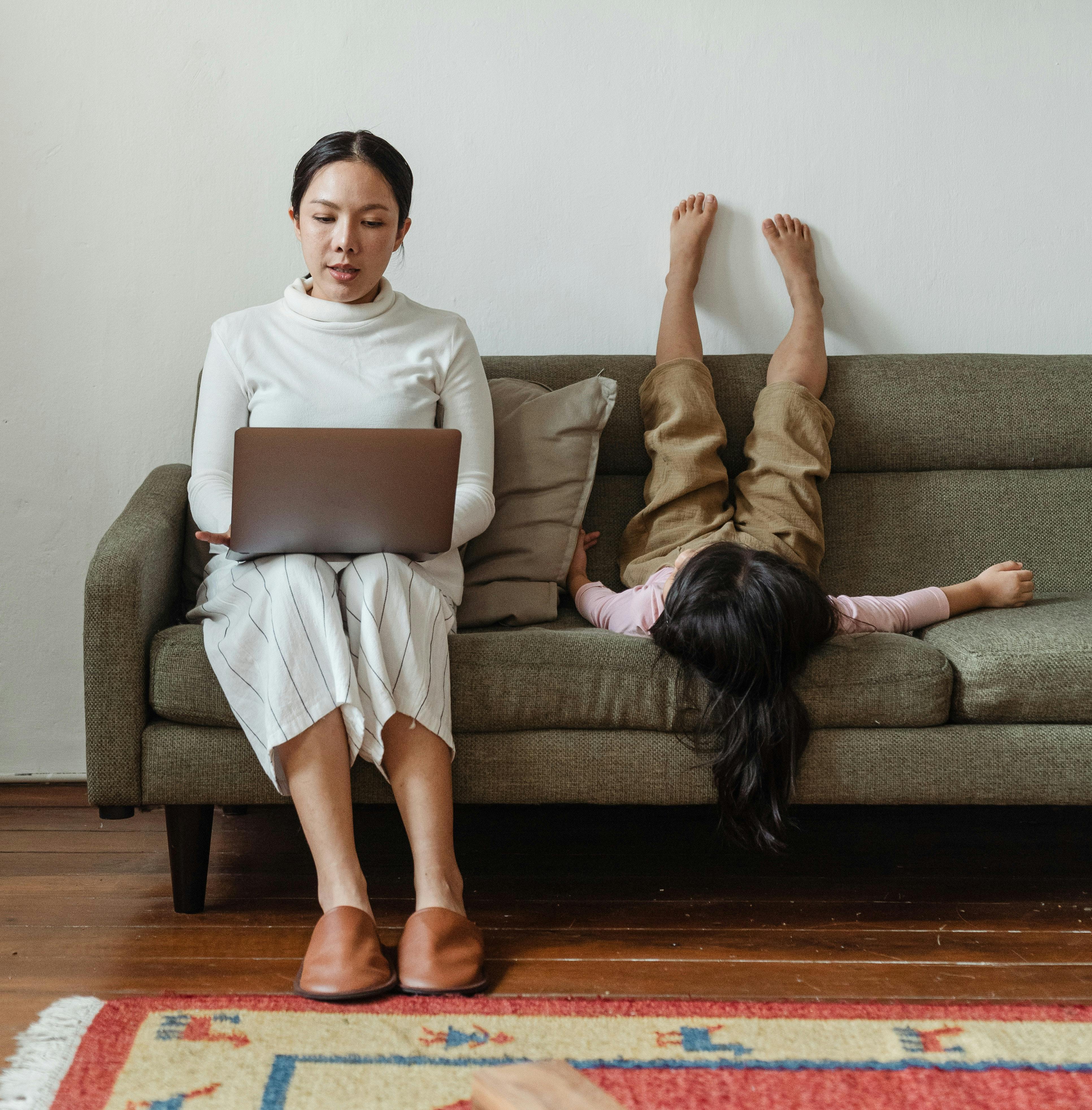 Woman on couch using laptop with daughter by her side