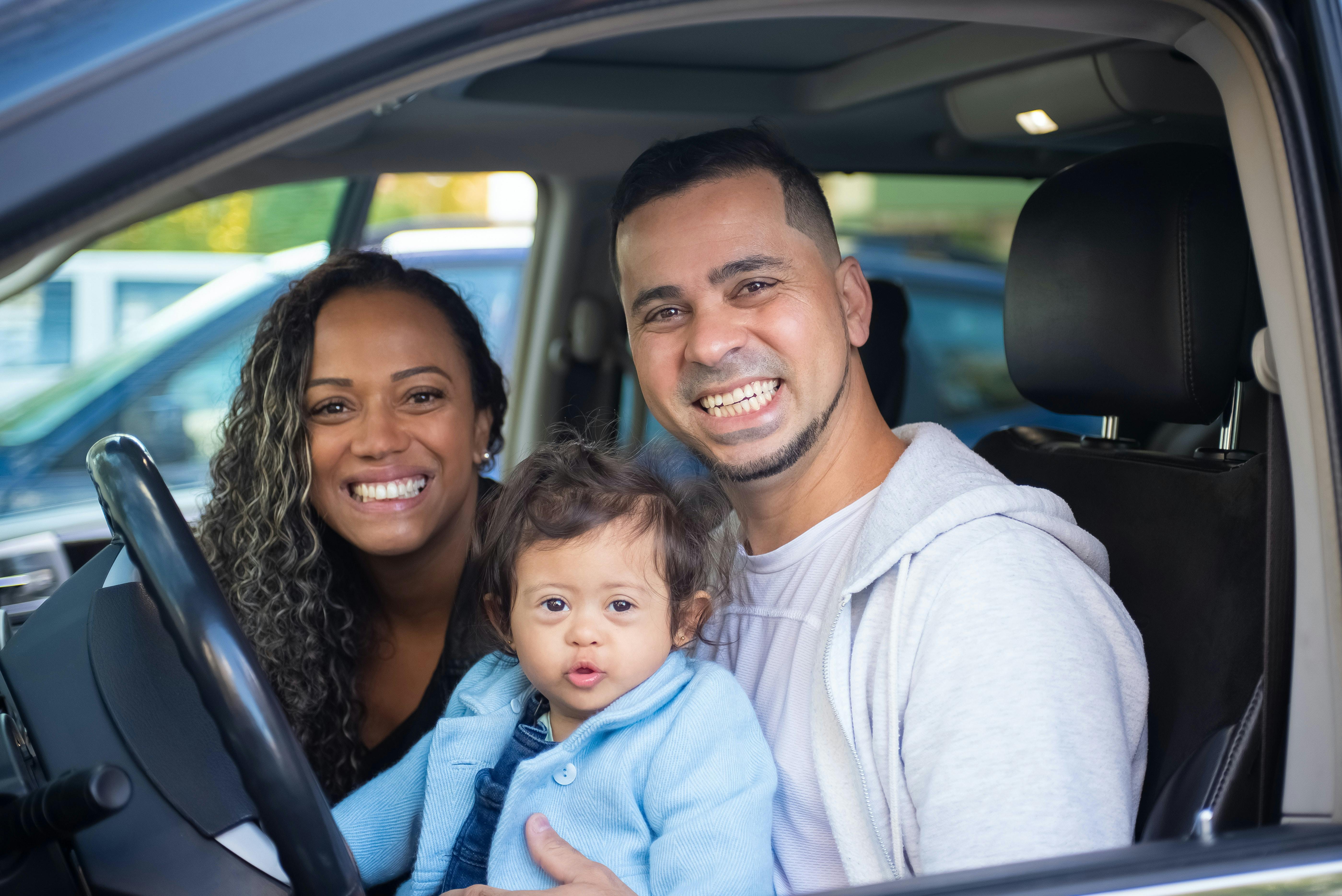 Couple with child smiling in seat of car