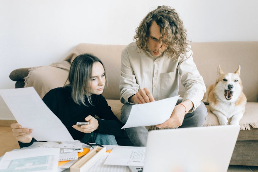 Couple with dog on couch reviewing documents with computer