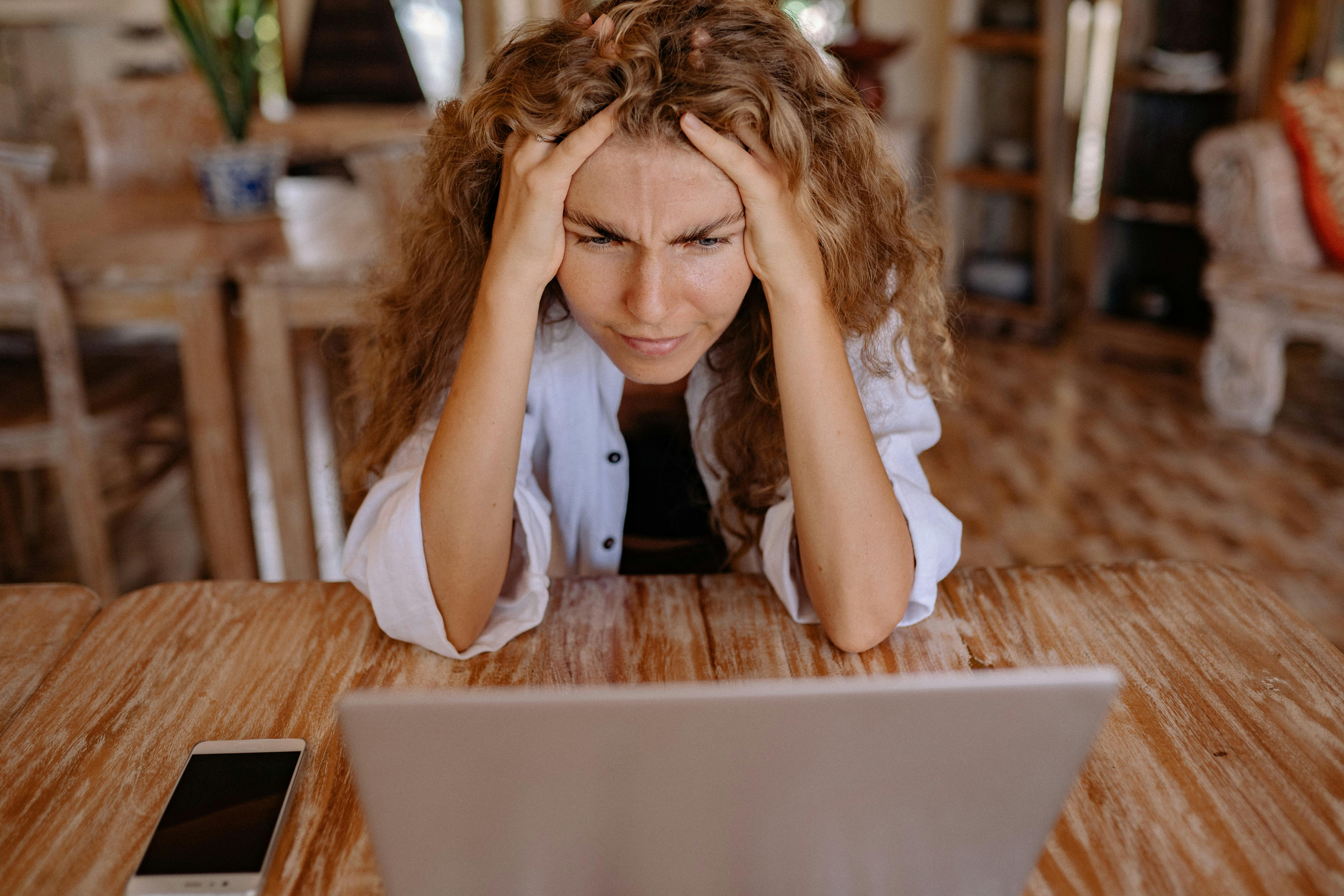 Woman frustrated staring at laptop with hands on head