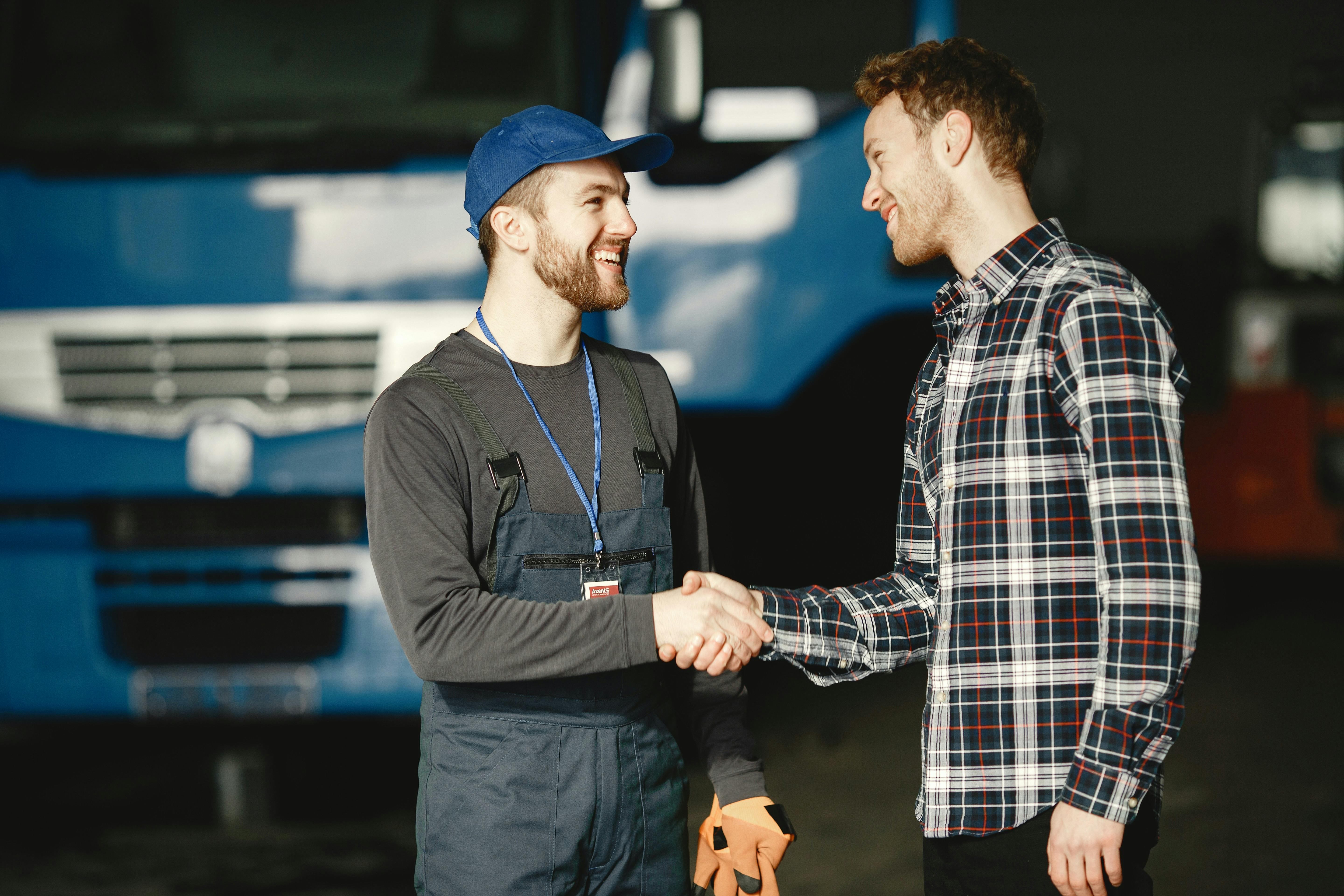 Tow men shaking hands and smiling in front of truck