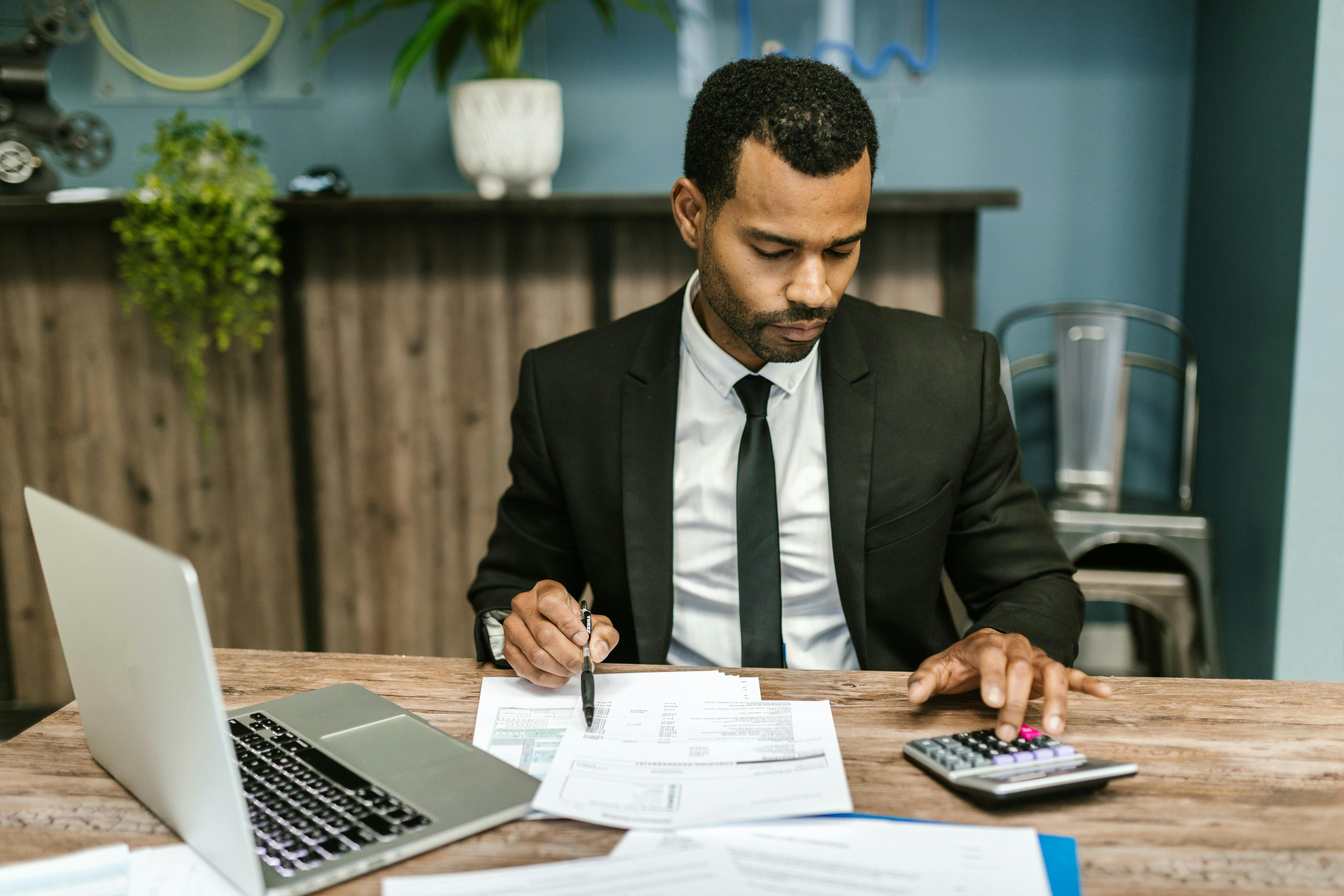 Man in suit at desk with laptop and calculator