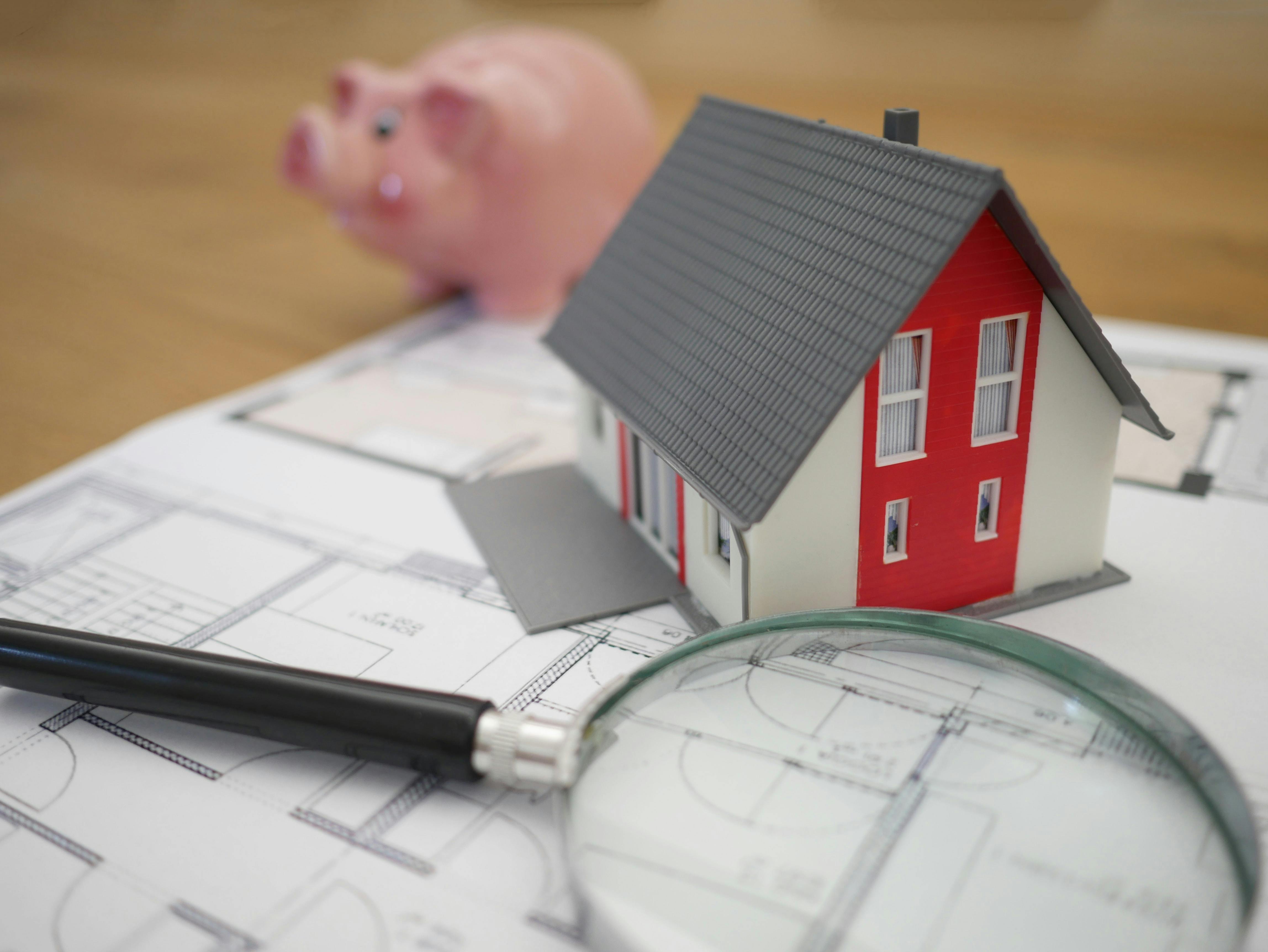 Model house with piggy bank and magnifying glass