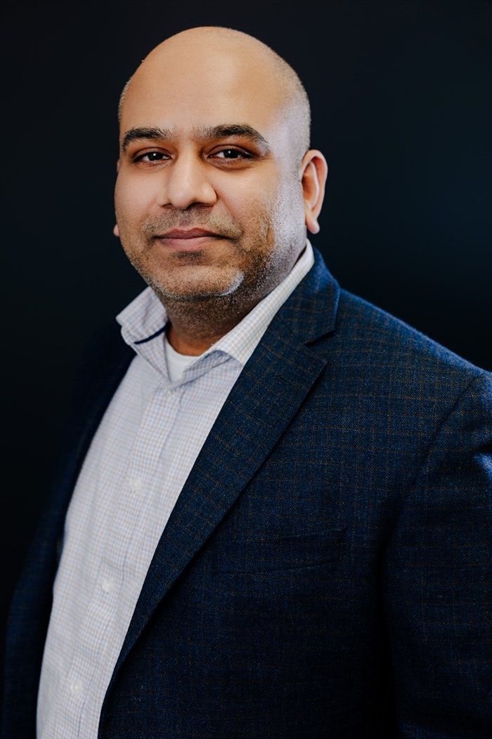 Portrait professionnel d’un homme portant une chemise pâle et un veston foncé, posé devant un fond noir.