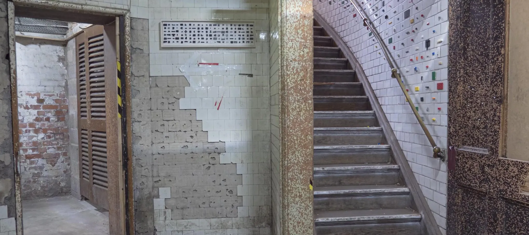 A tiled stairwell in a former magistrates’ court, LEGO pieces set into the white tile grid