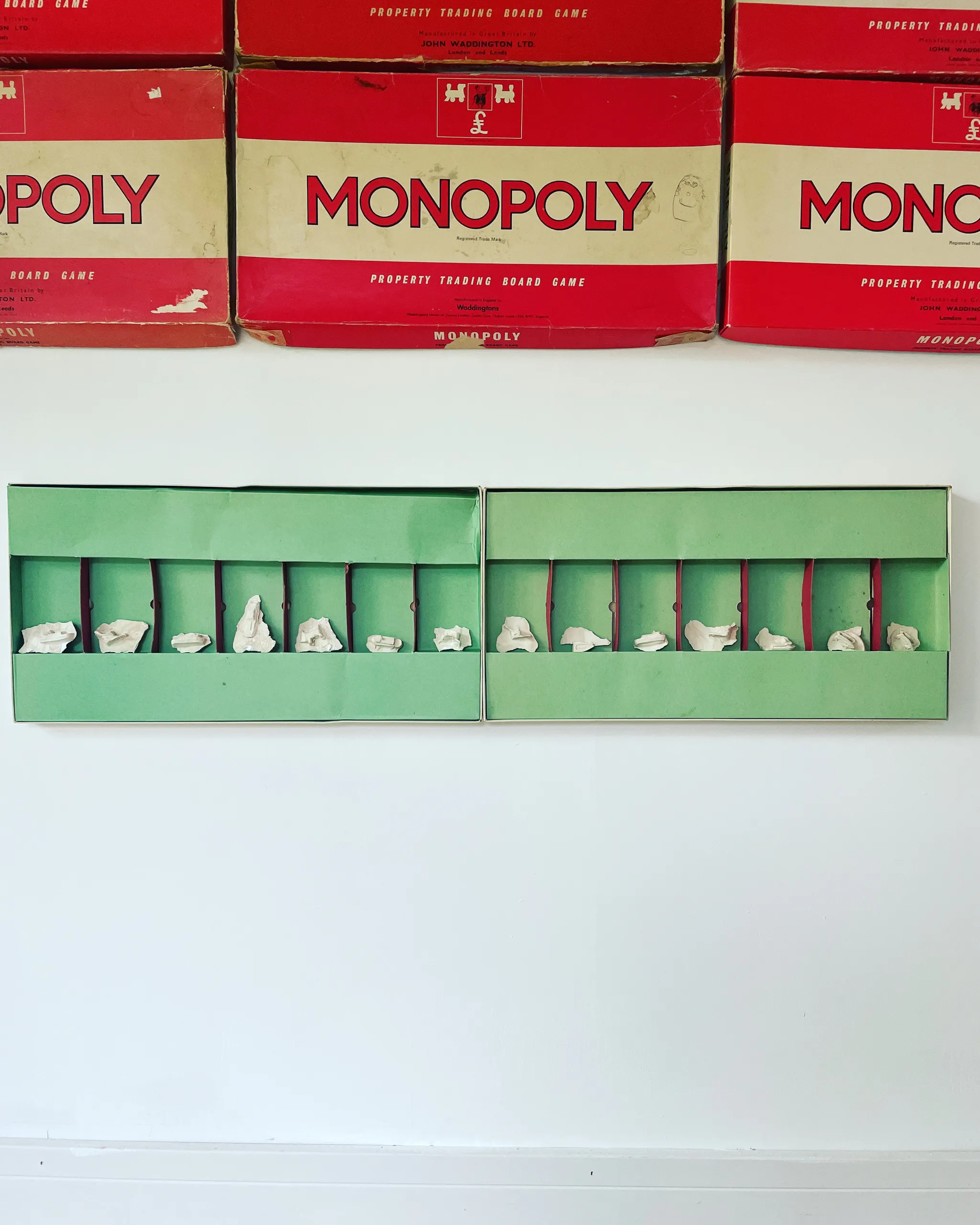 Green box trays mounted on a wall beneath stacked Monopoly boxes