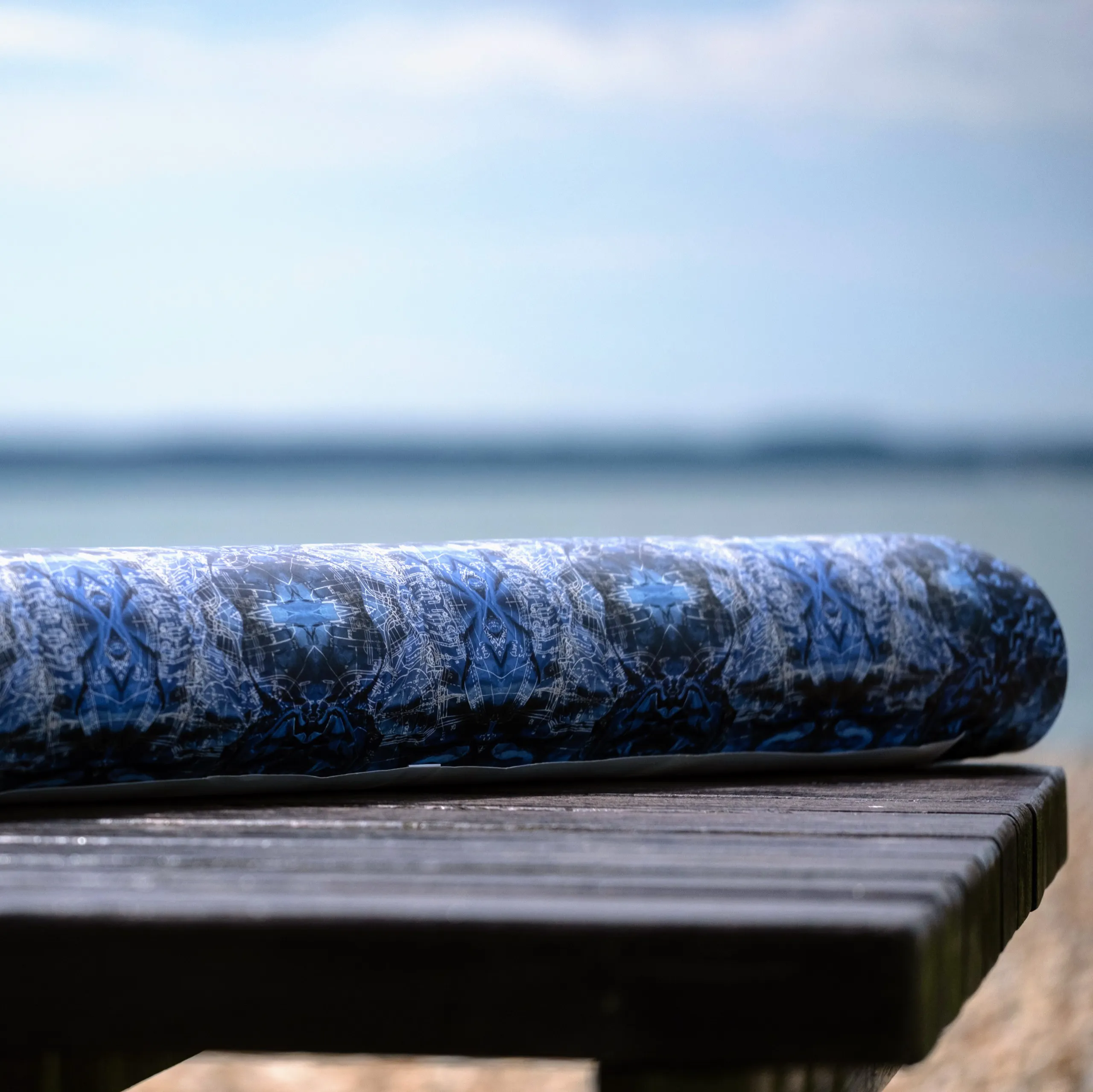A rolled bolt of printed cloth resting on a weathered bench by the water